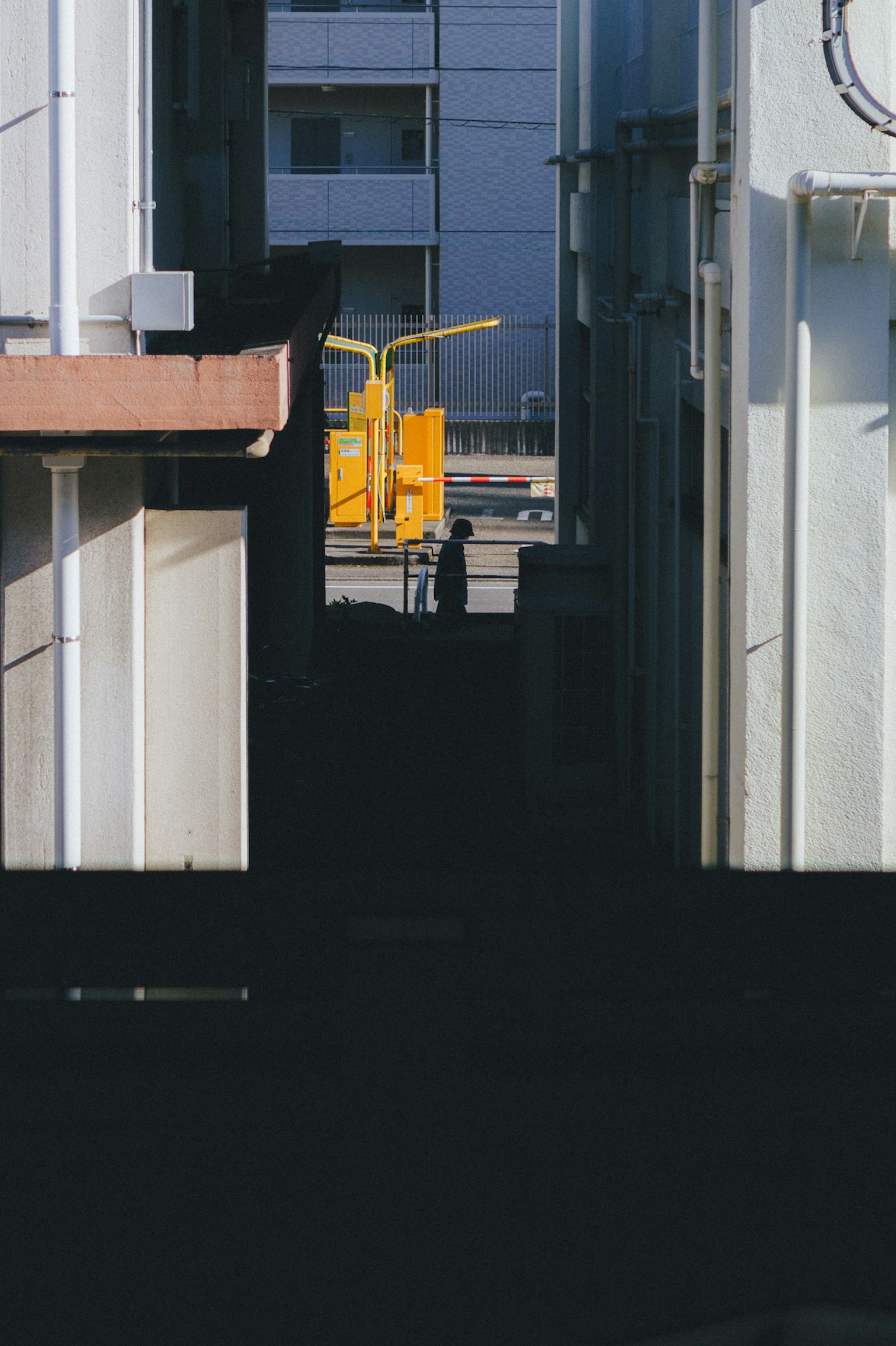 Silhouette of a person standing in a narrow alley with a yellow crane
