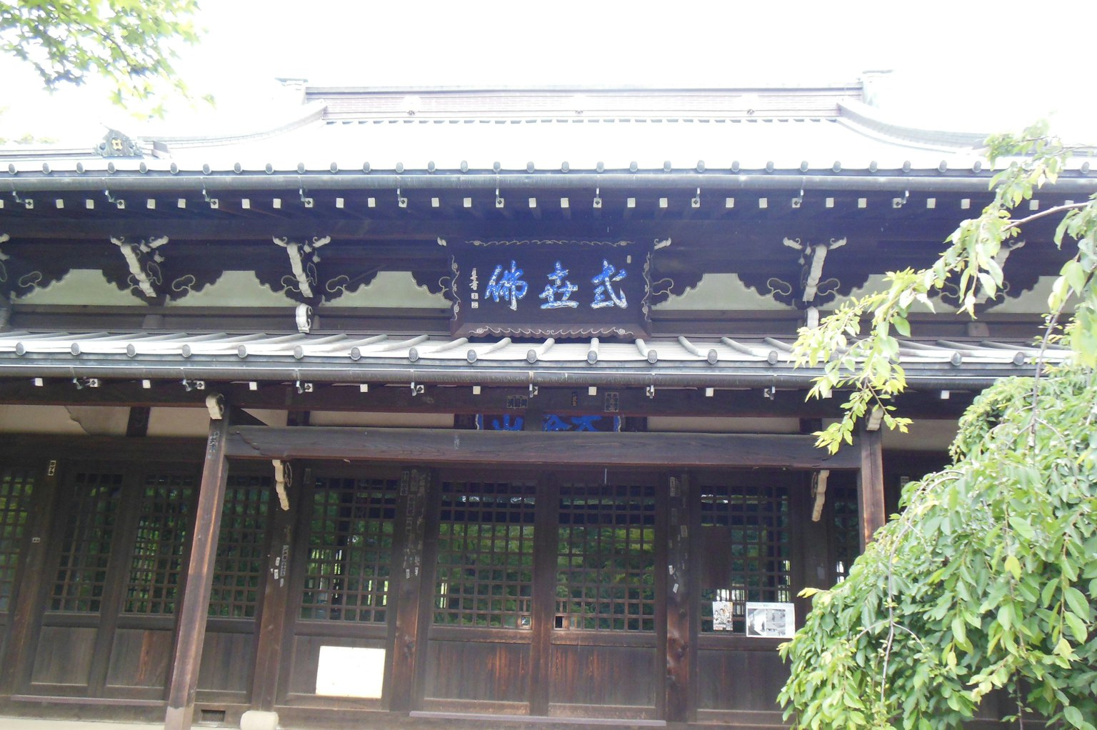 Traditional Japanese building exterior with wooden structure and decorative roof featuring blue sign with kanji characters