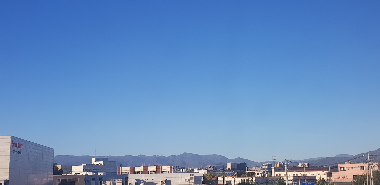 Langit biru cerah di atas pemandangan kota dengan pegunungan di latar belakang