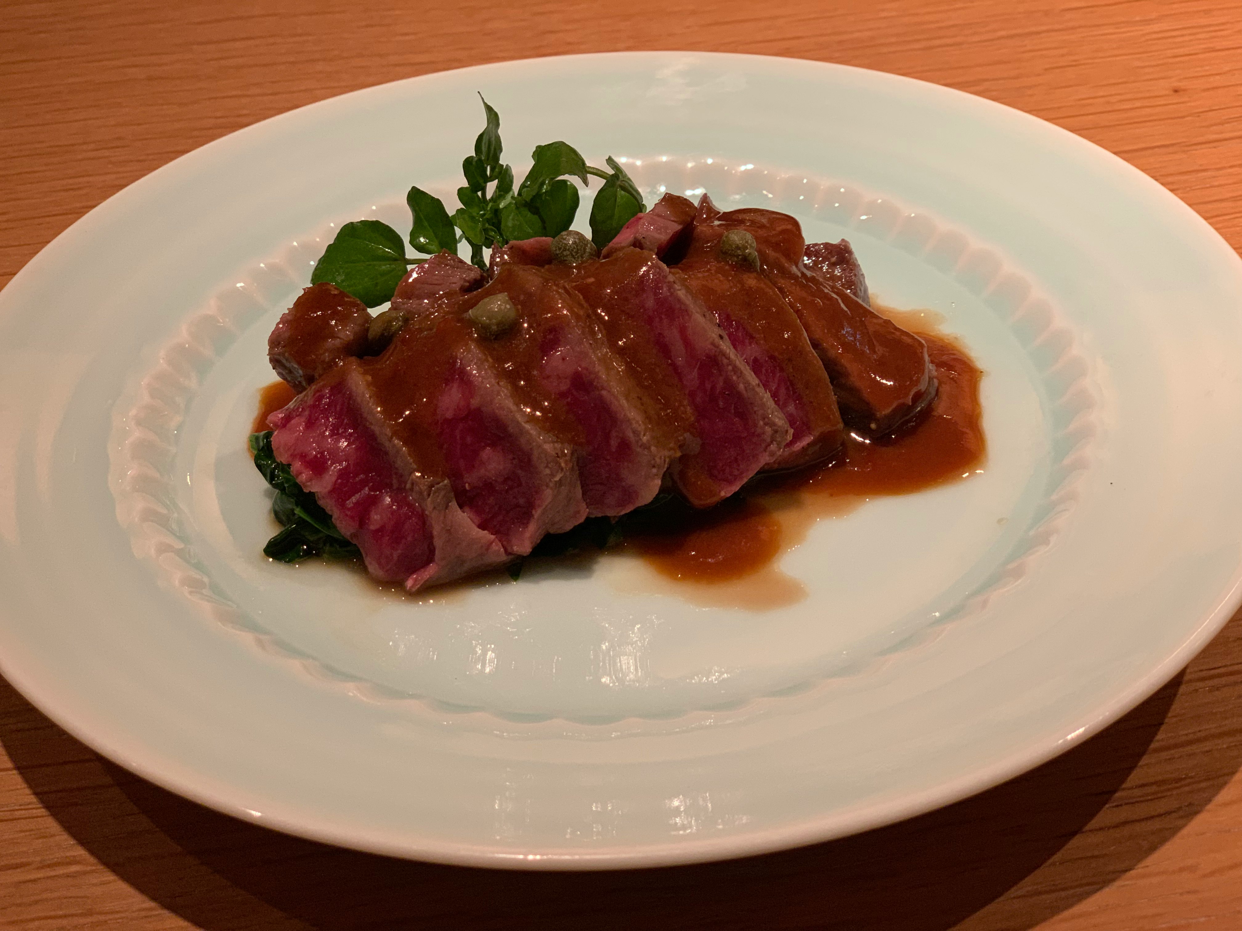 A beautifully plated dish of sliced meat with sauce and greens