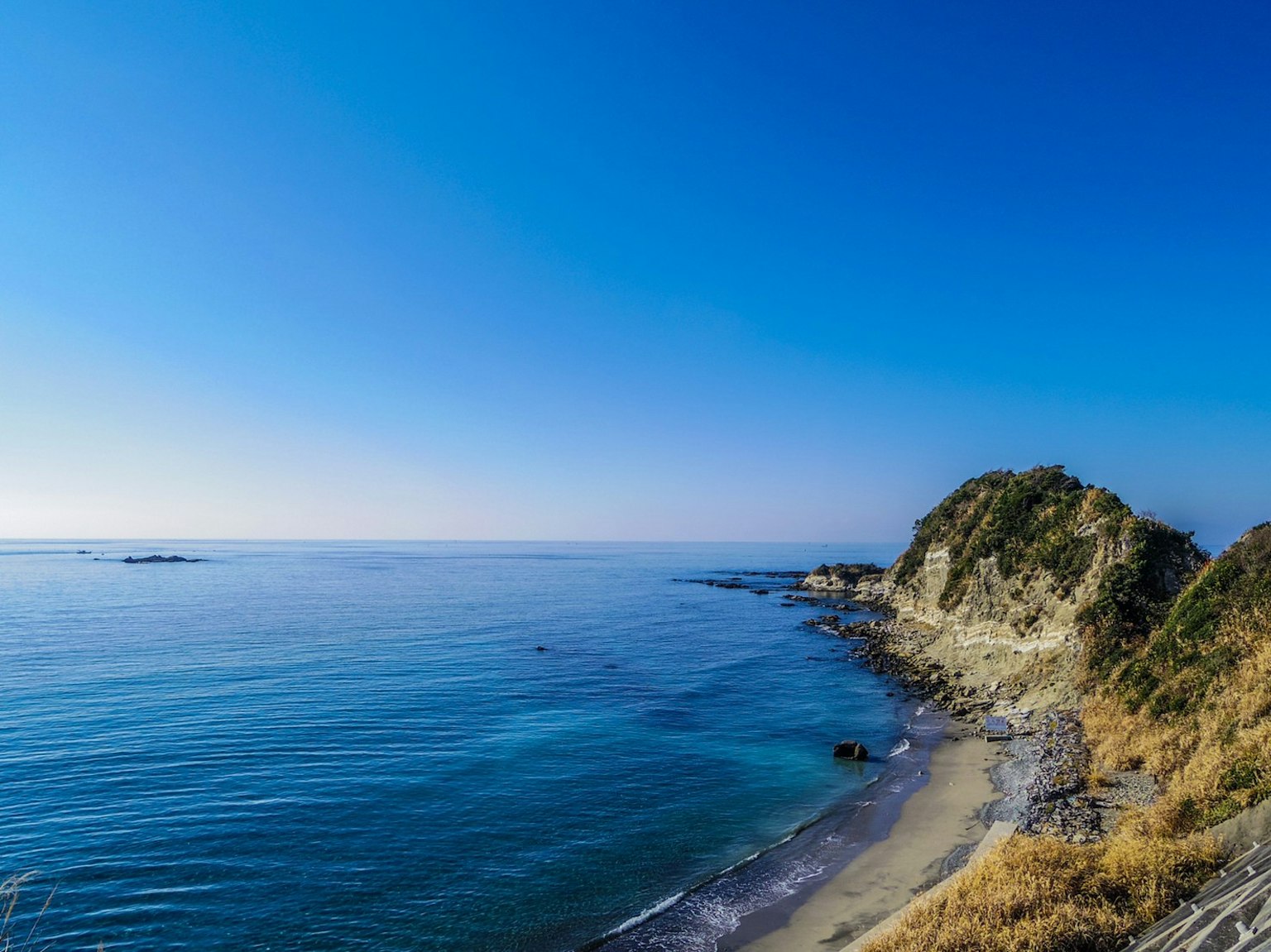 Vista panoramica di una spiaggia di sabbia e una costa rocciosa sotto un cielo blu chiaro