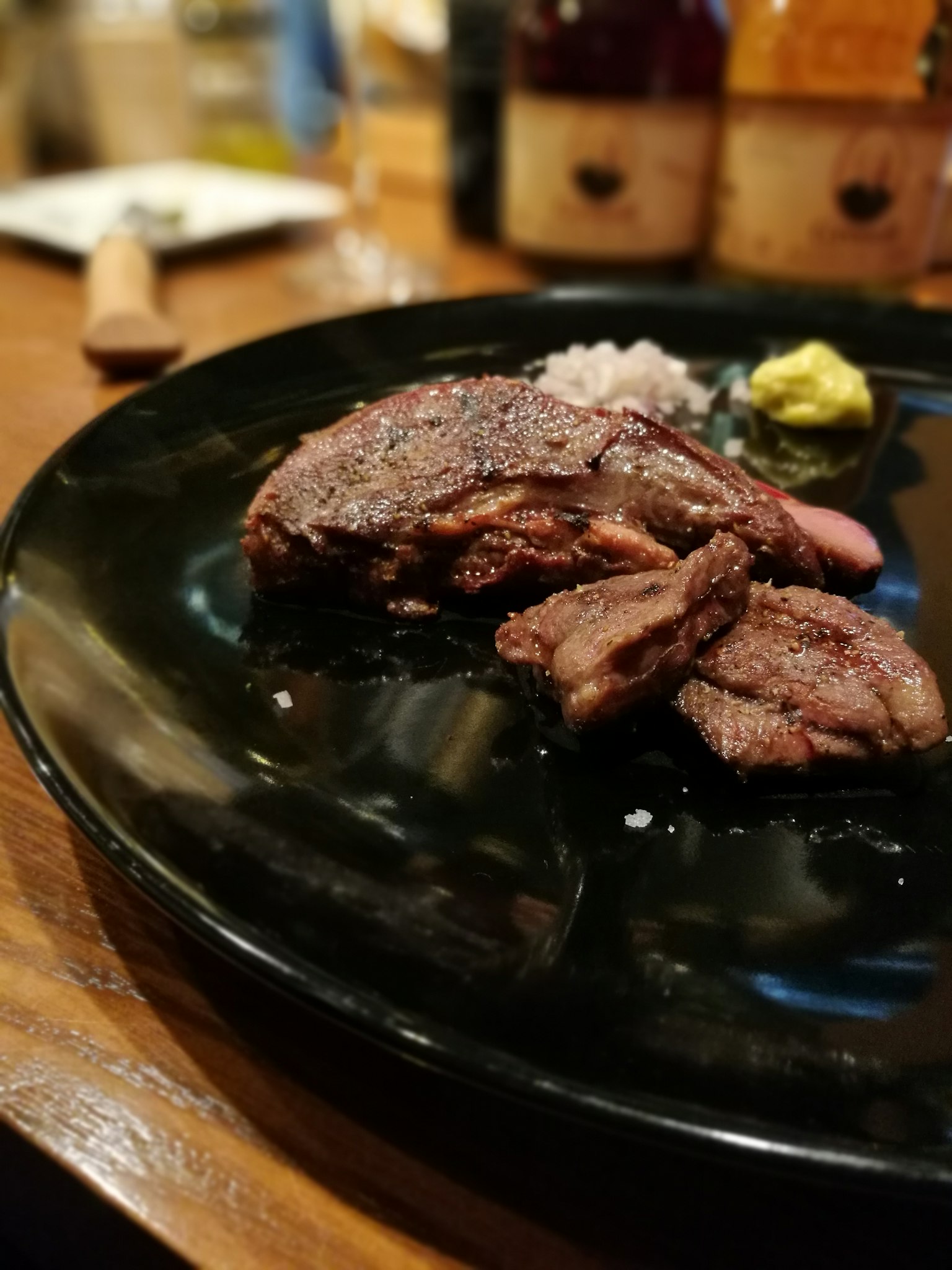 Scheiben von gegrilltem Fleisch auf einem schwarzen Teller mit Wasabi und Salz