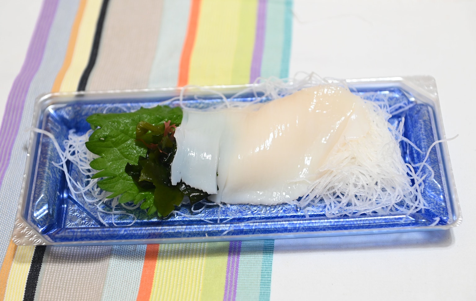 Sashimi segar disajikan di piring biru dengan daun hijau