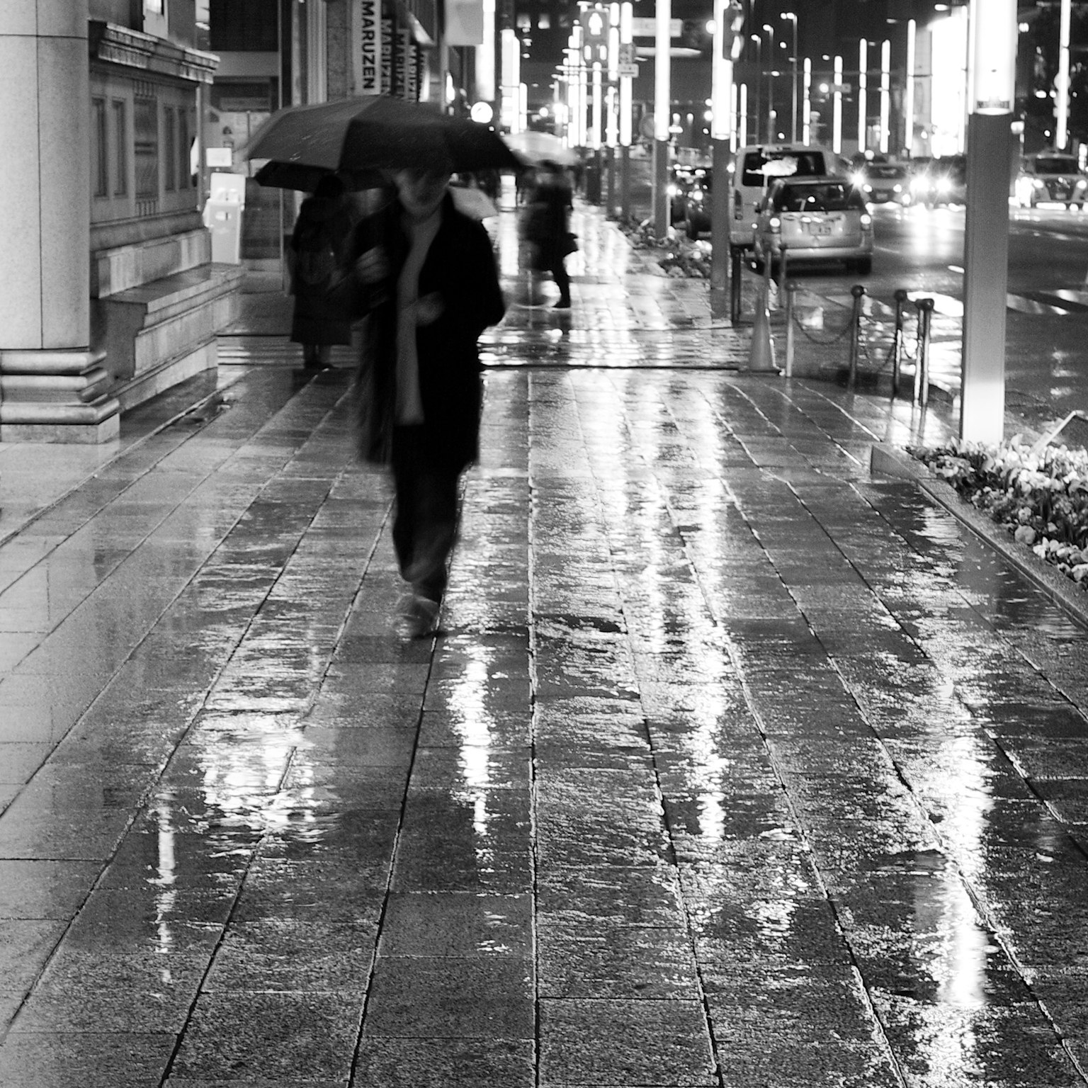 Silhouette di persone che camminano su un marciapiede bagnato dalla pioggia di notte con ombrelli