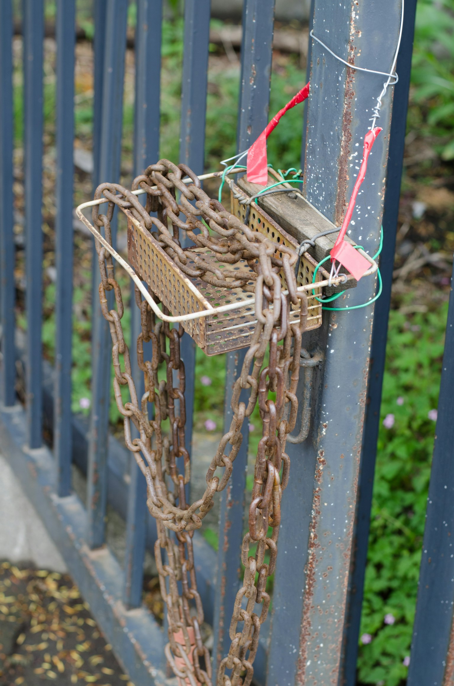 Rusty chains hanging from a metal box attached to a fence