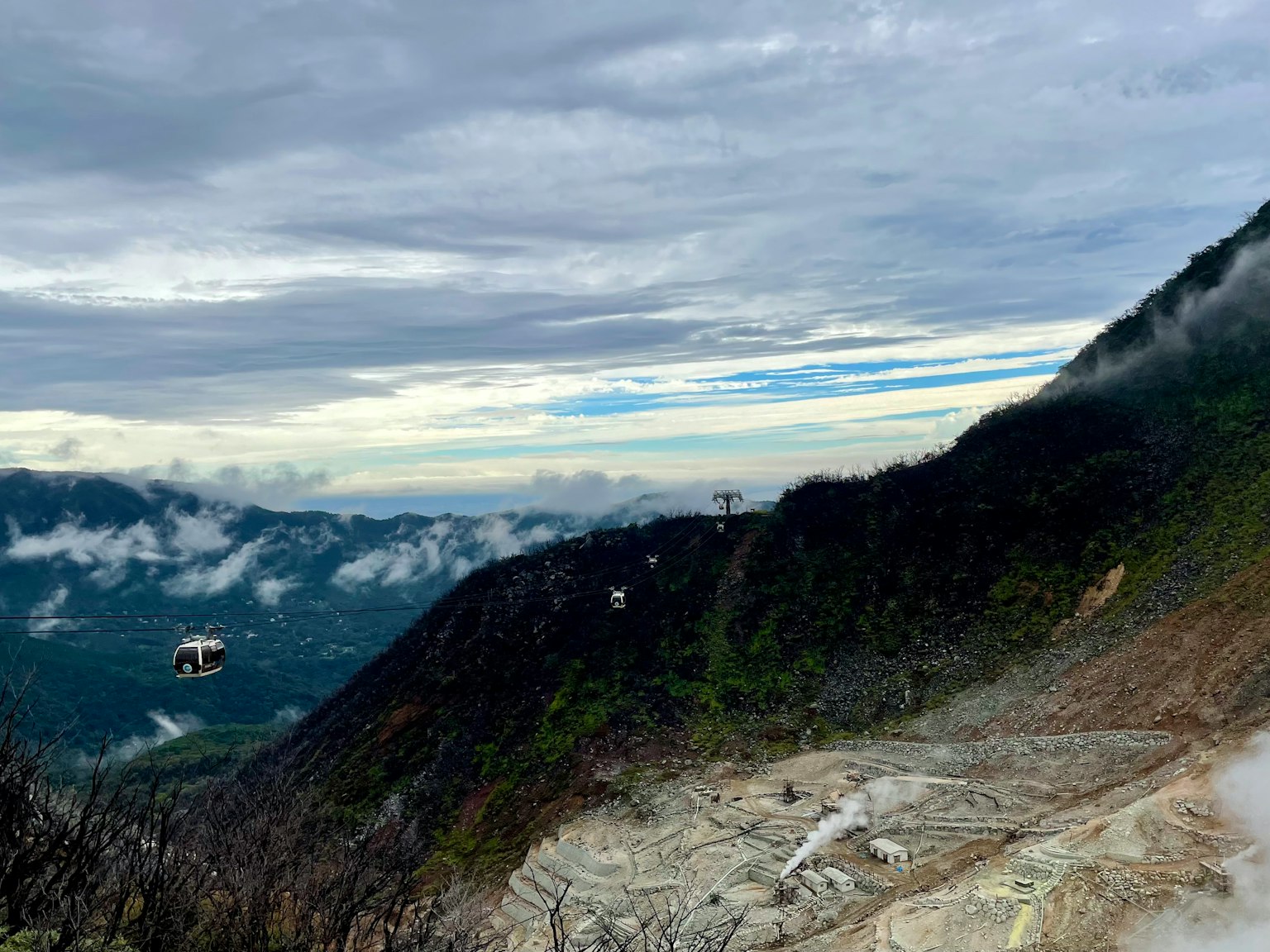 Kabel gantung di lereng gunung dengan awan menutupi bukit