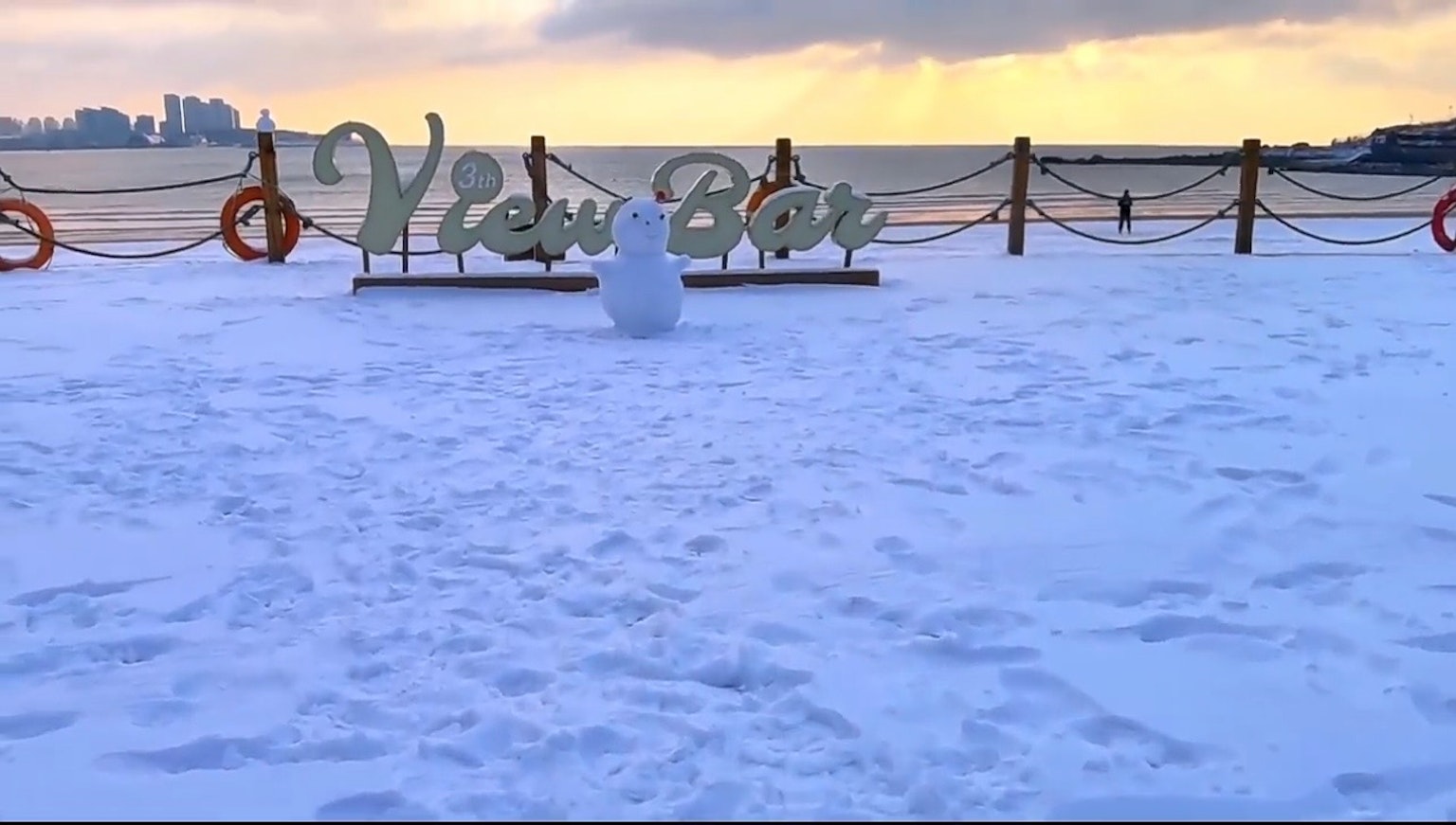 被雪覆盖的海滩上有一个'View Bar'标志和一个雪人
