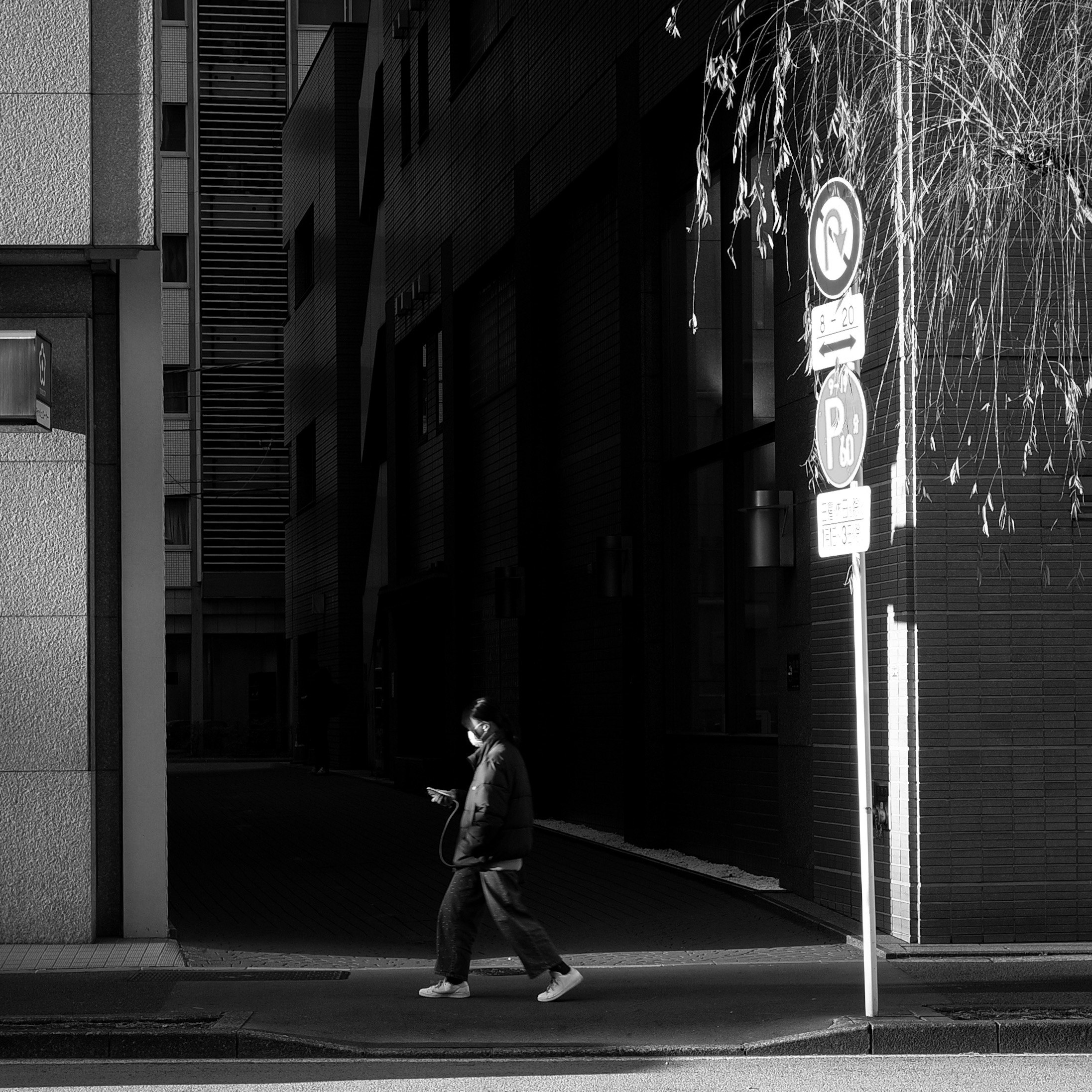 西日が差す路地を歩く人のモノクロ風景