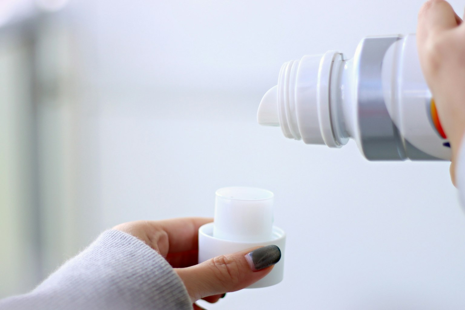 Nahaufnahme einer Hand, die Creme aus einer weißen Flasche in einen kleinen Behälter gießt