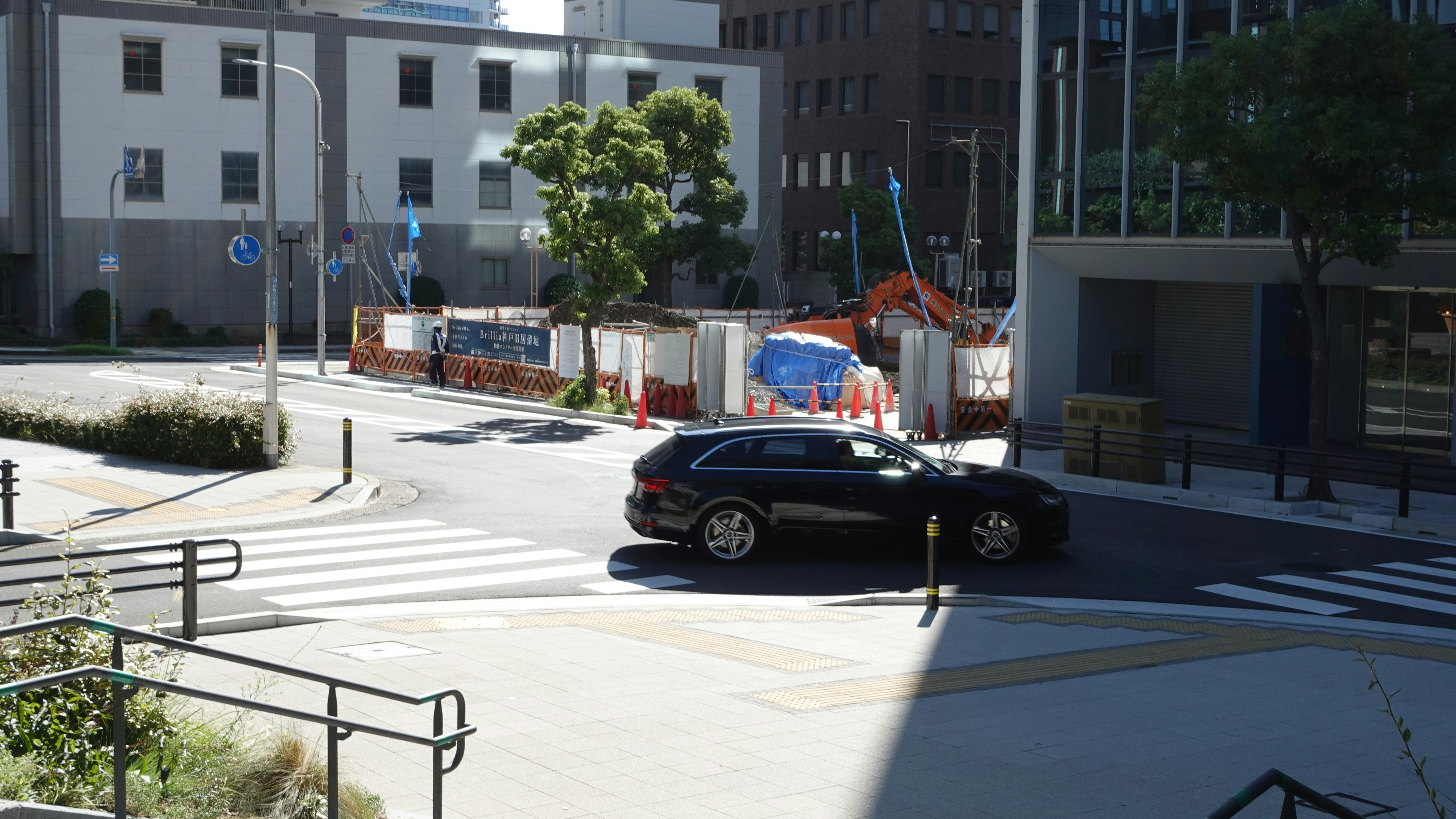 Black car stopped at an urban intersection beside construction fencing