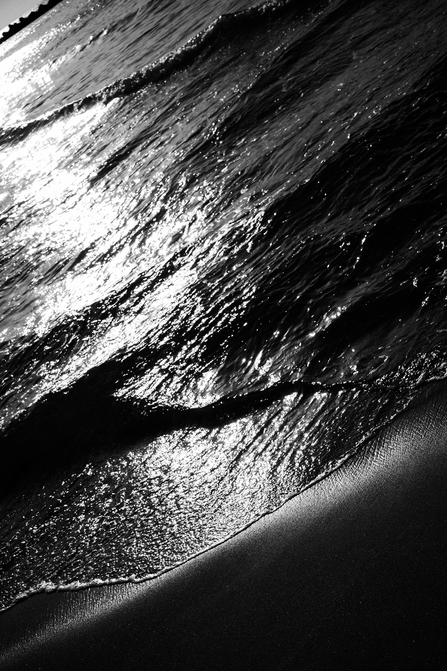 波が砂浜に打ち寄せるモノクロの画像 光の反射が美しい