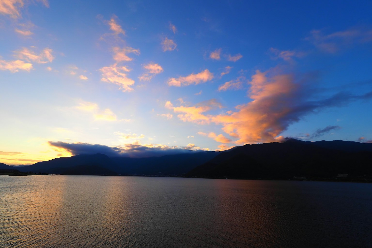 Lago tranquilo reflejando un cielo de atardecer y montañas