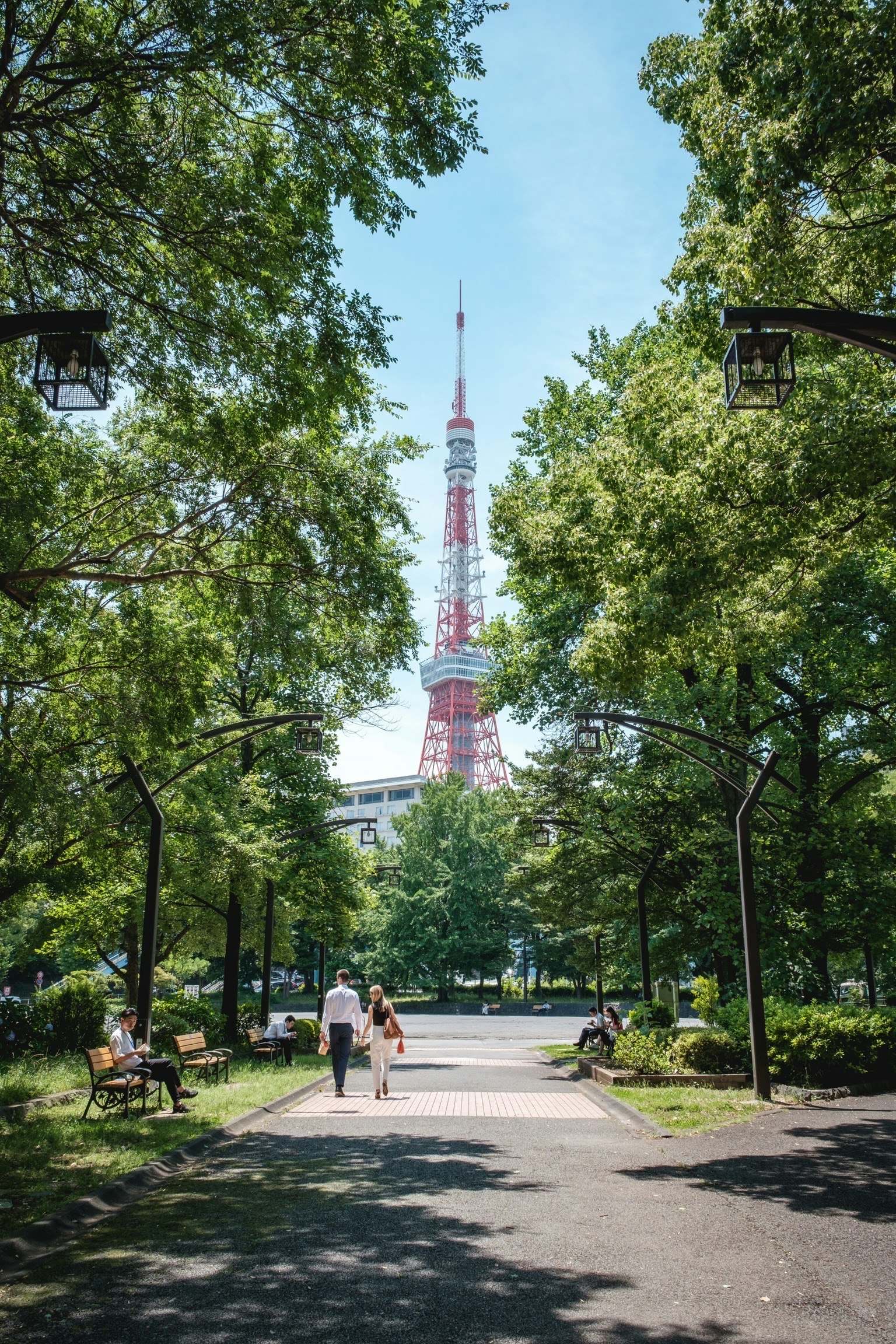 Personas caminando por un sendero en un parque frondoso con la Torre de Tokio al fondo