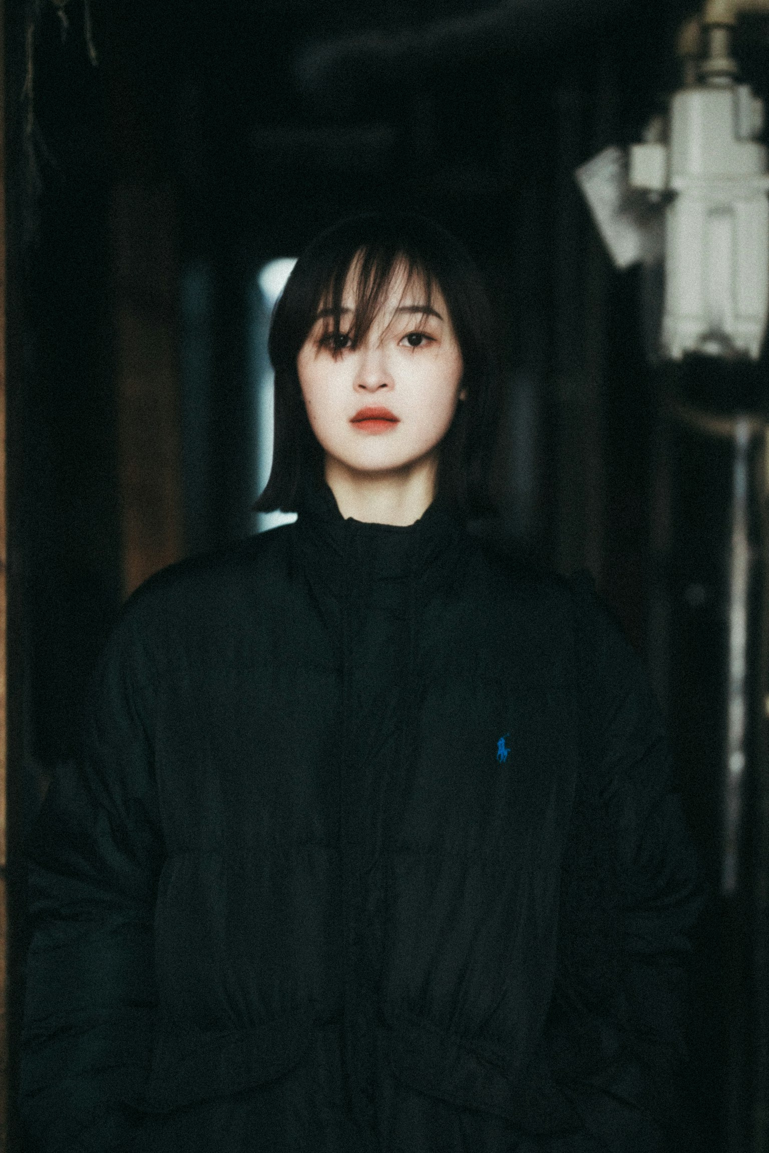 A woman wearing a black coat standing in a dimly lit space