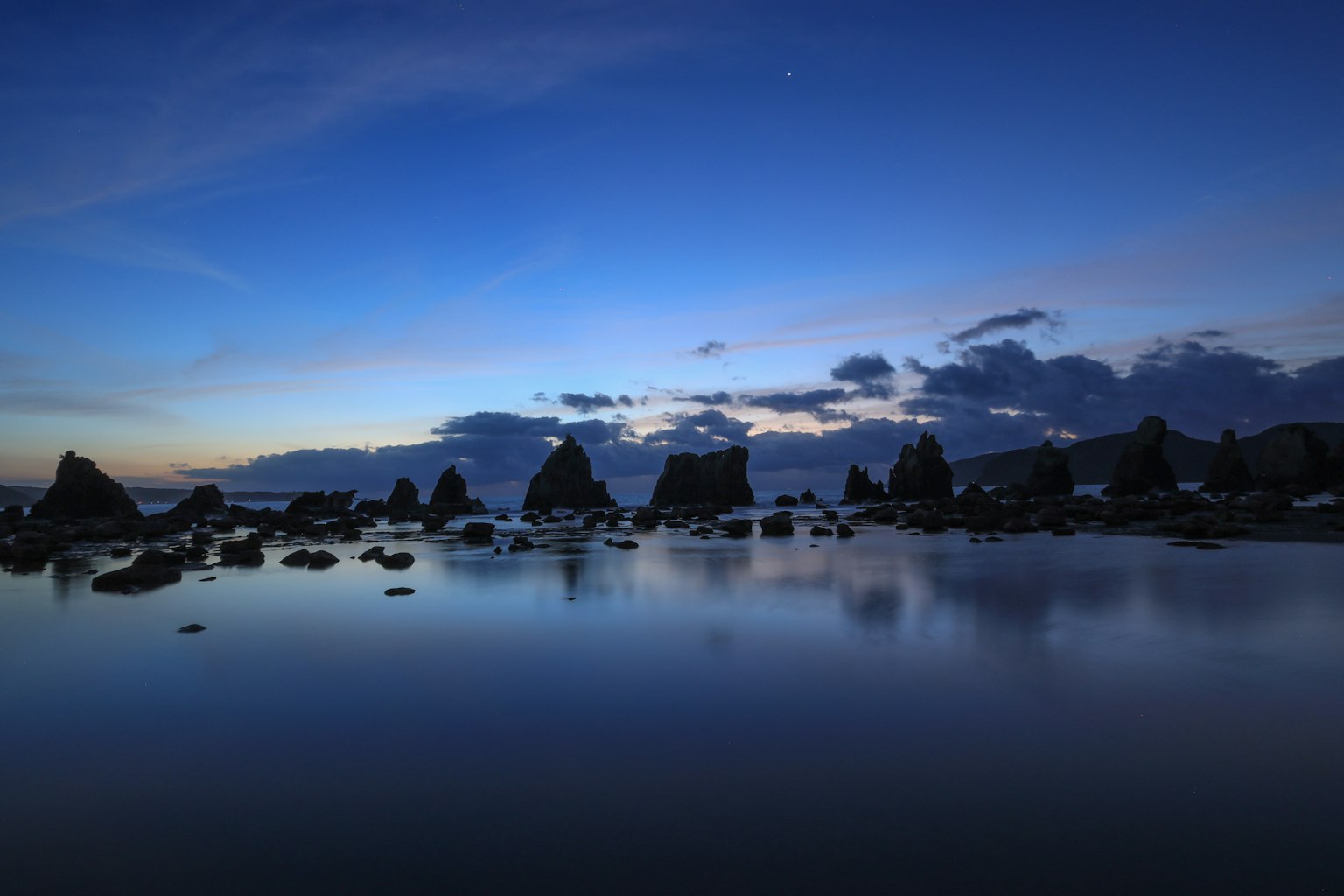 平静的海岸风景，岩石在蓝色黄昏天空的映衬下显得轮廓分明