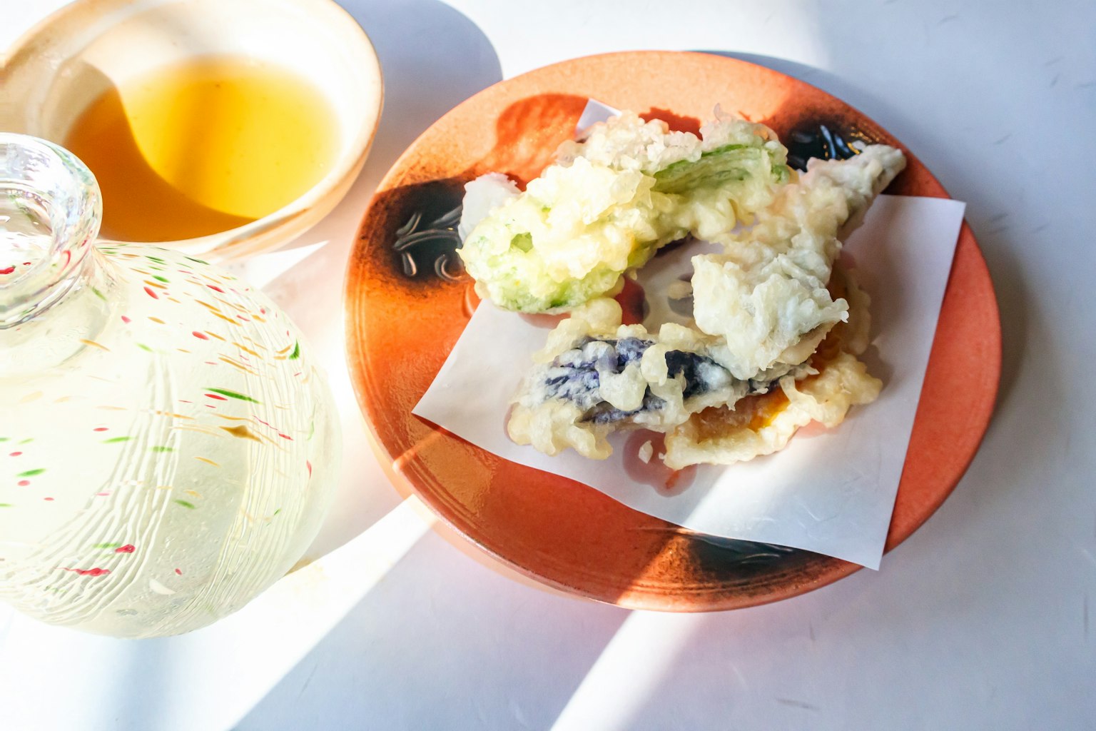 Một đĩa với tempura và rau củ đa dạng bên cạnh một tách trà