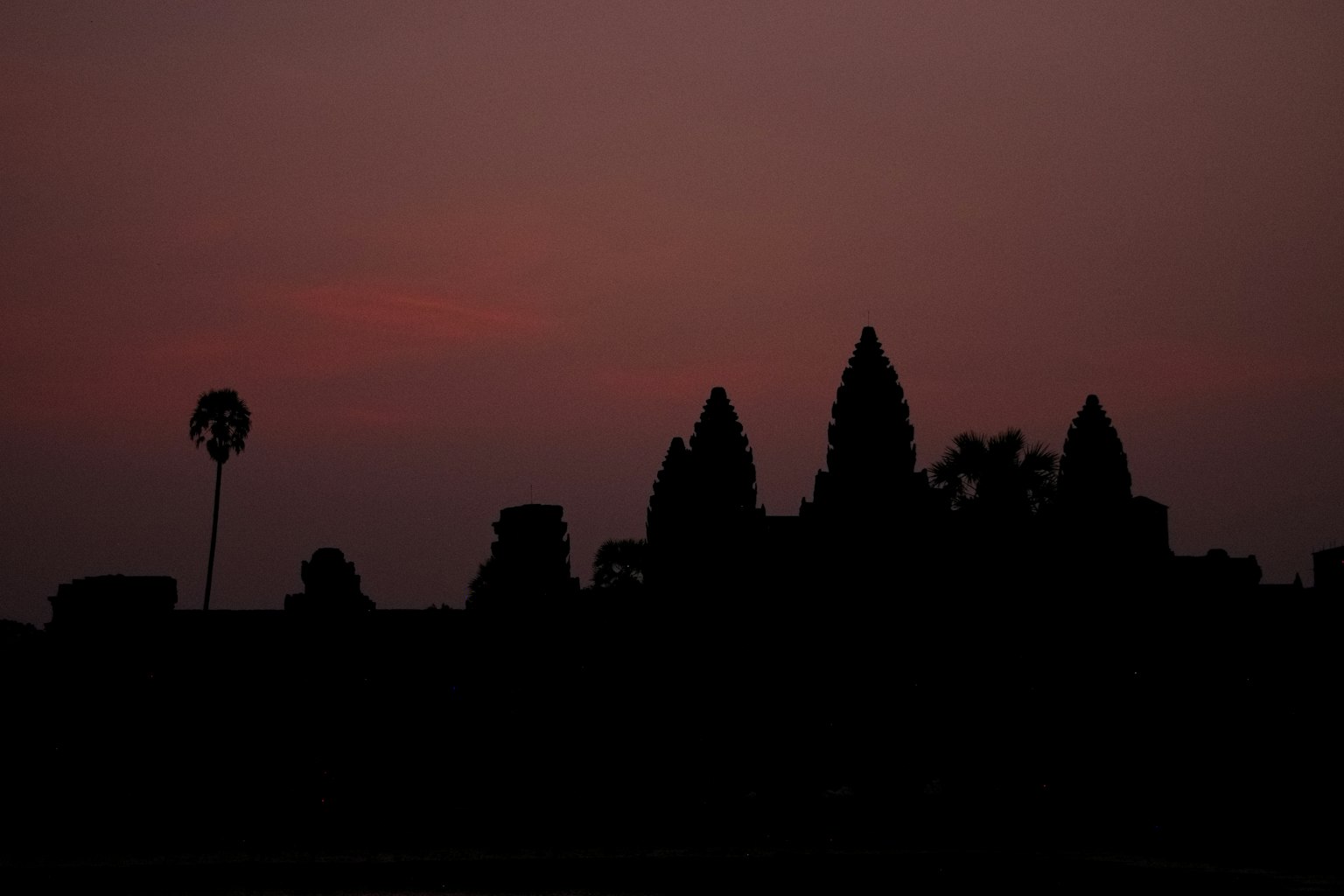 Silhouette of Angkor Wat at dusk with palm trees
