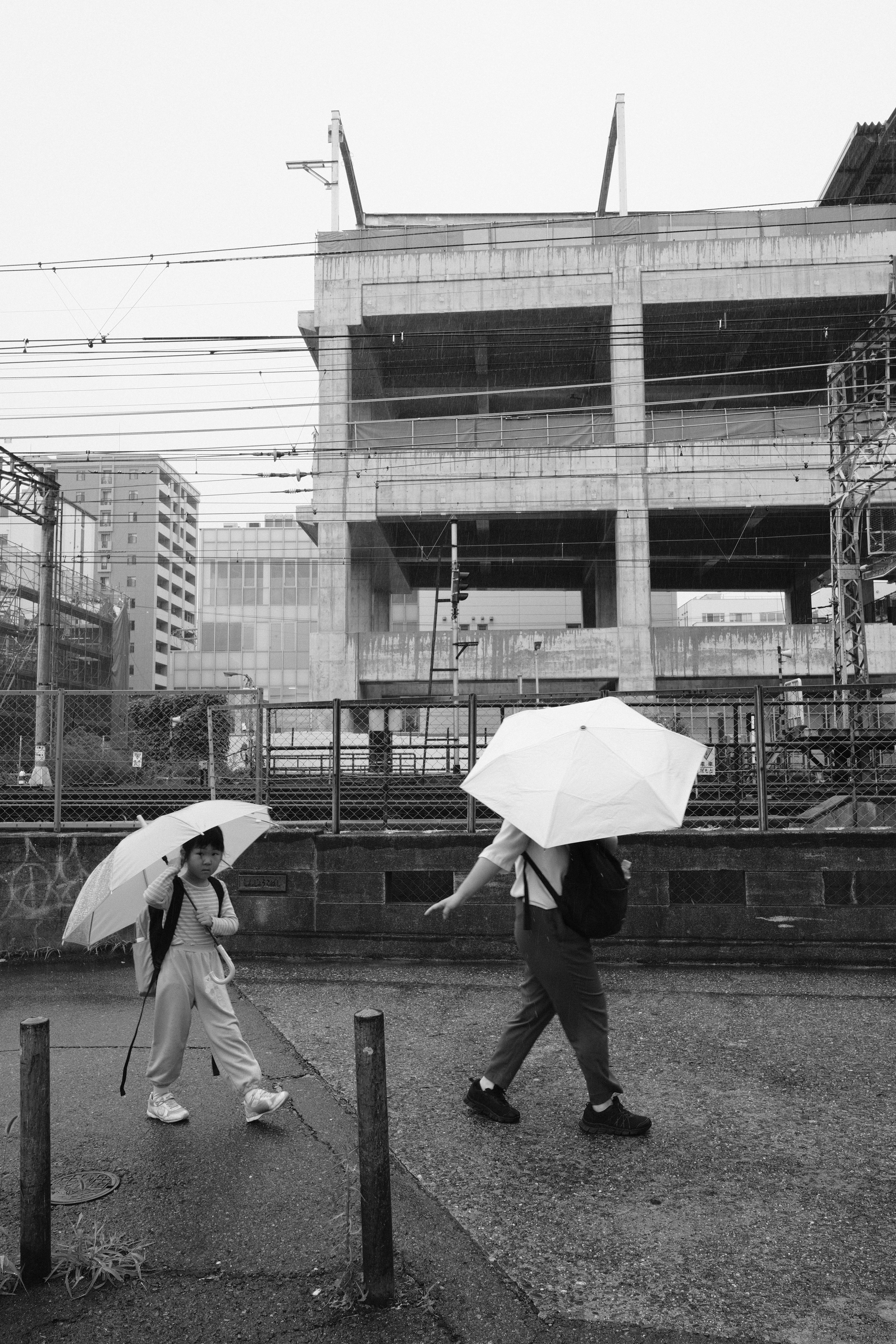 雨の中、傘をさして歩く人と工事中の建物