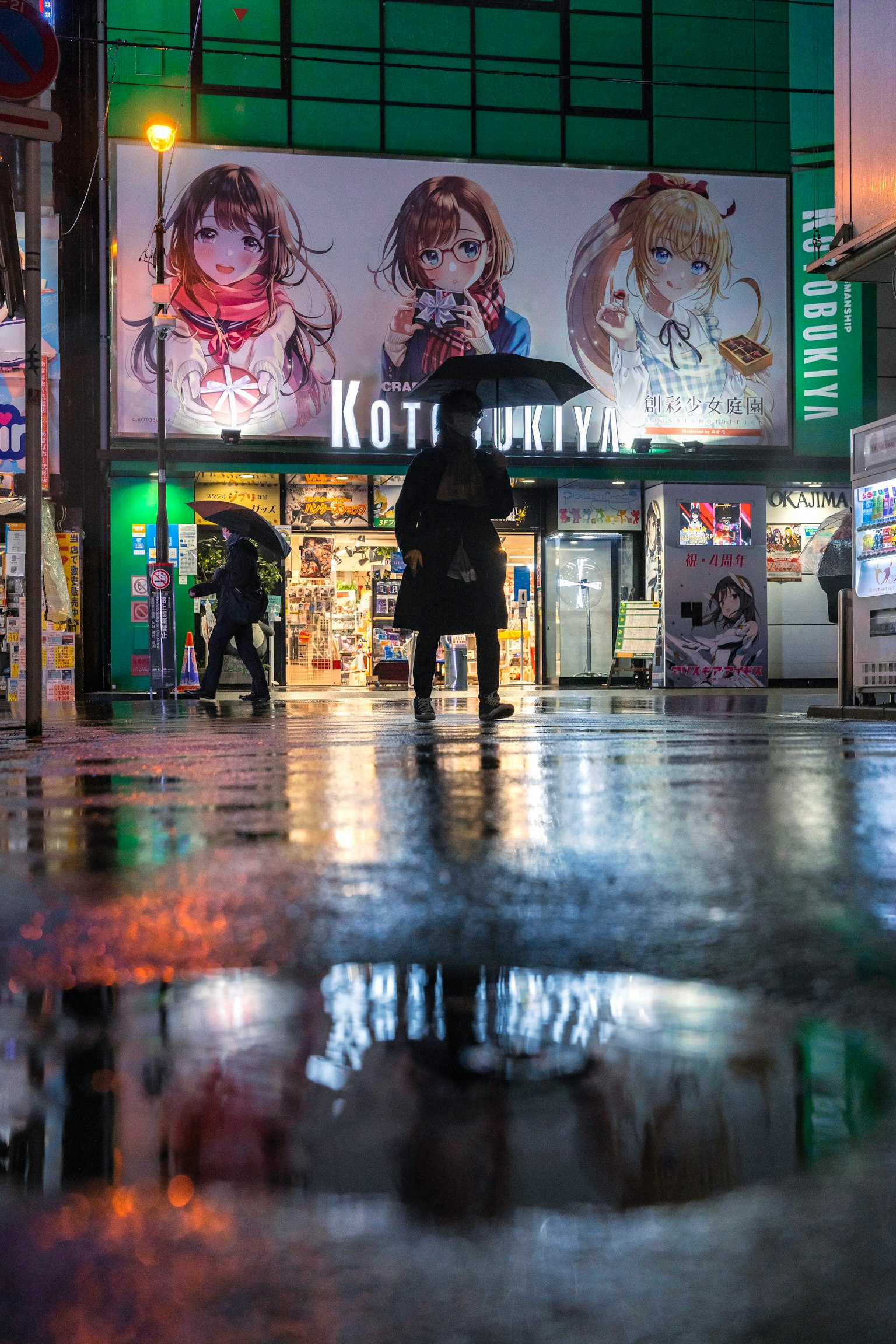 Una persona con un ombrello sotto la pioggia con manifesti di anime in una scena di strada affollata