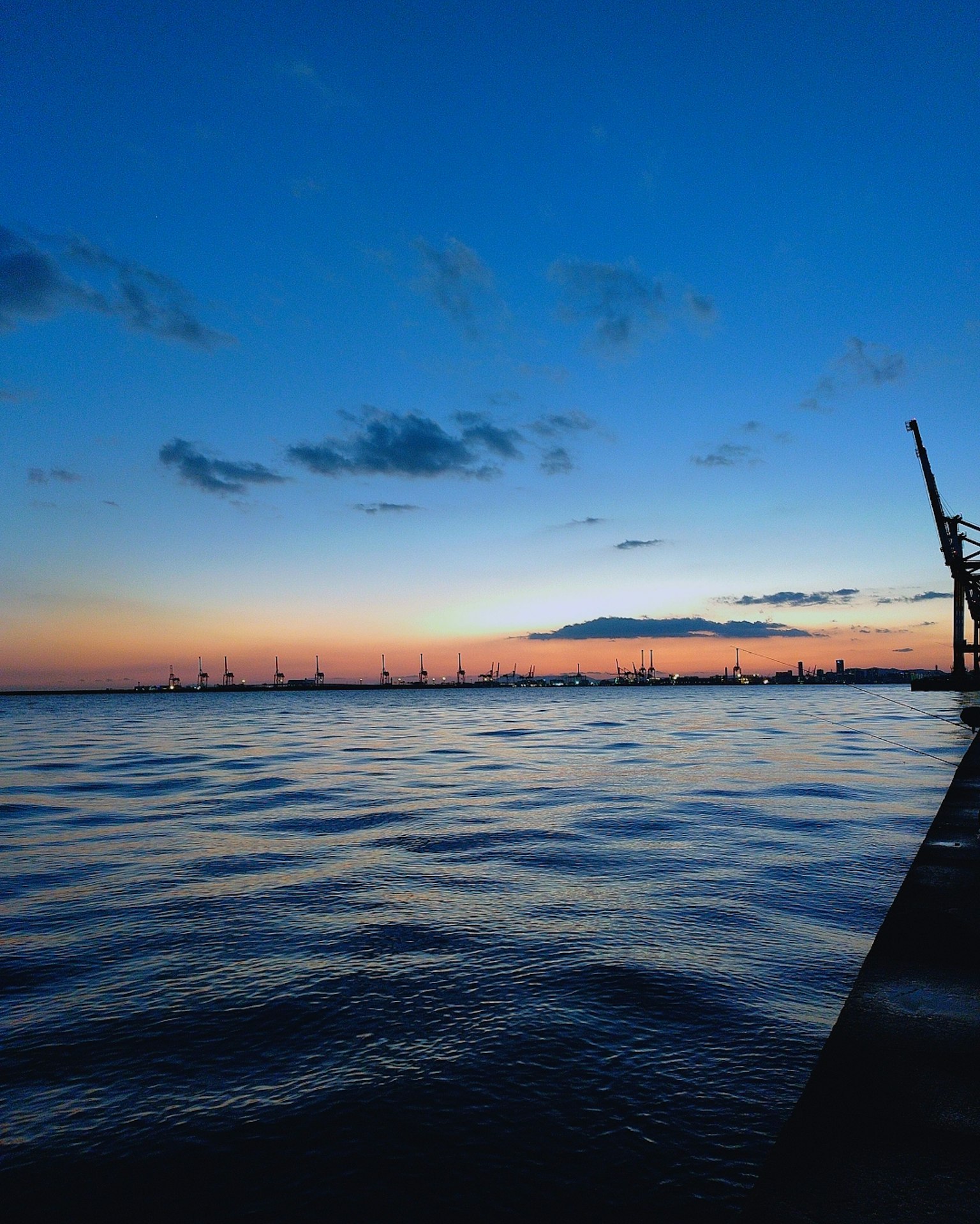 Atardecer sobre aguas tranquilas con grúas en el puerto