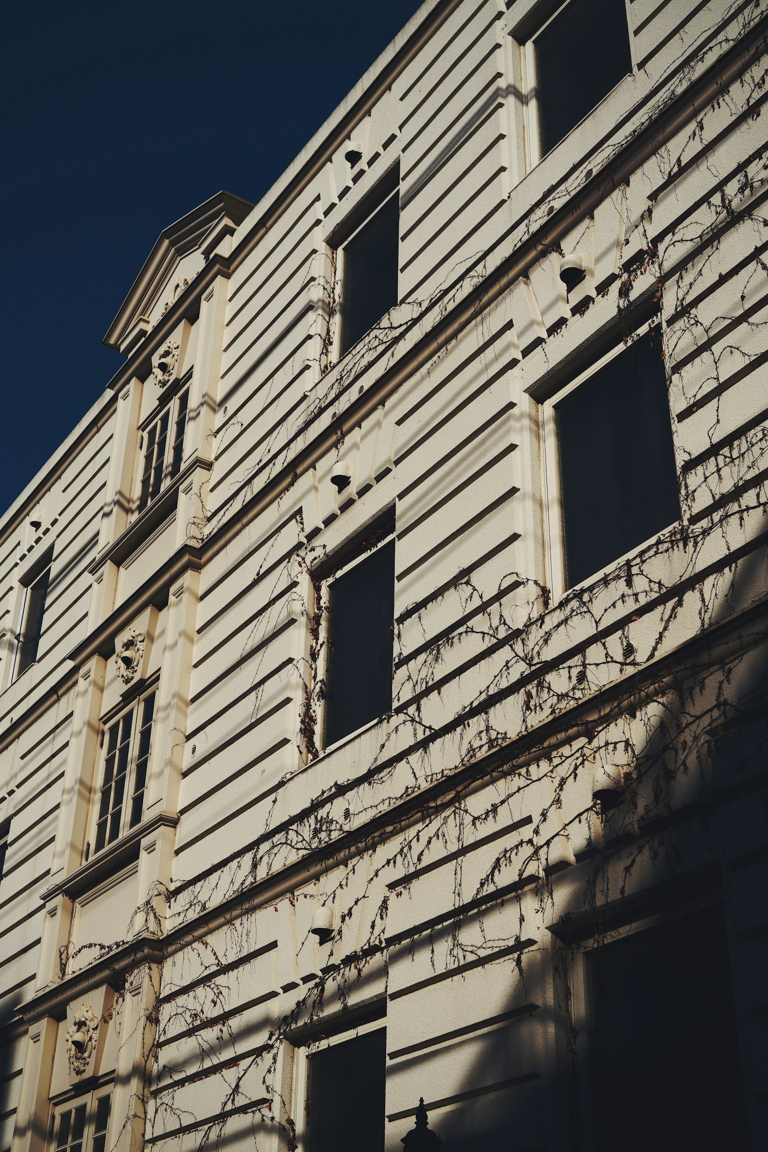 Ein historisches Gebäude mit einer weißen Fassade und mehreren Fenstern, die Schatten werfen