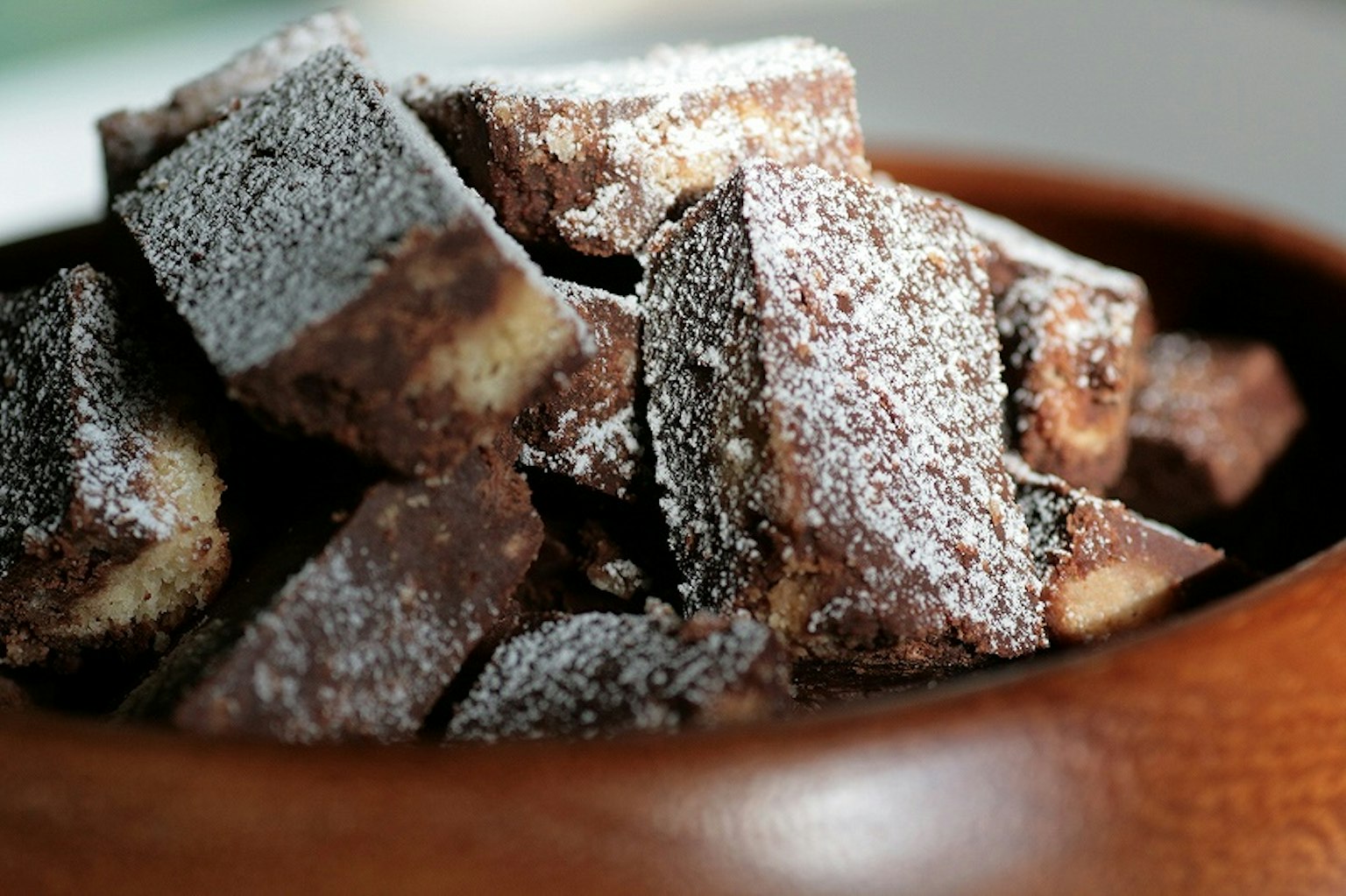 Potongan kue cokelat yang ditaburi gula bubuk dalam mangkuk kayu