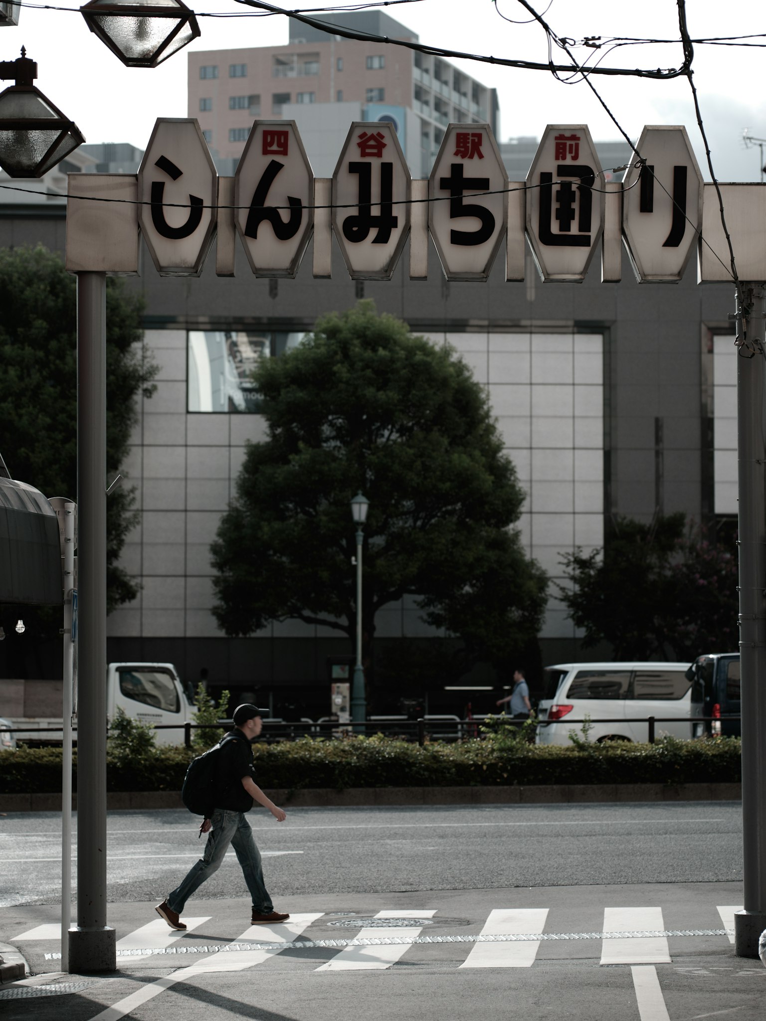 A person crossing the street under a traditional sign in a cityscape