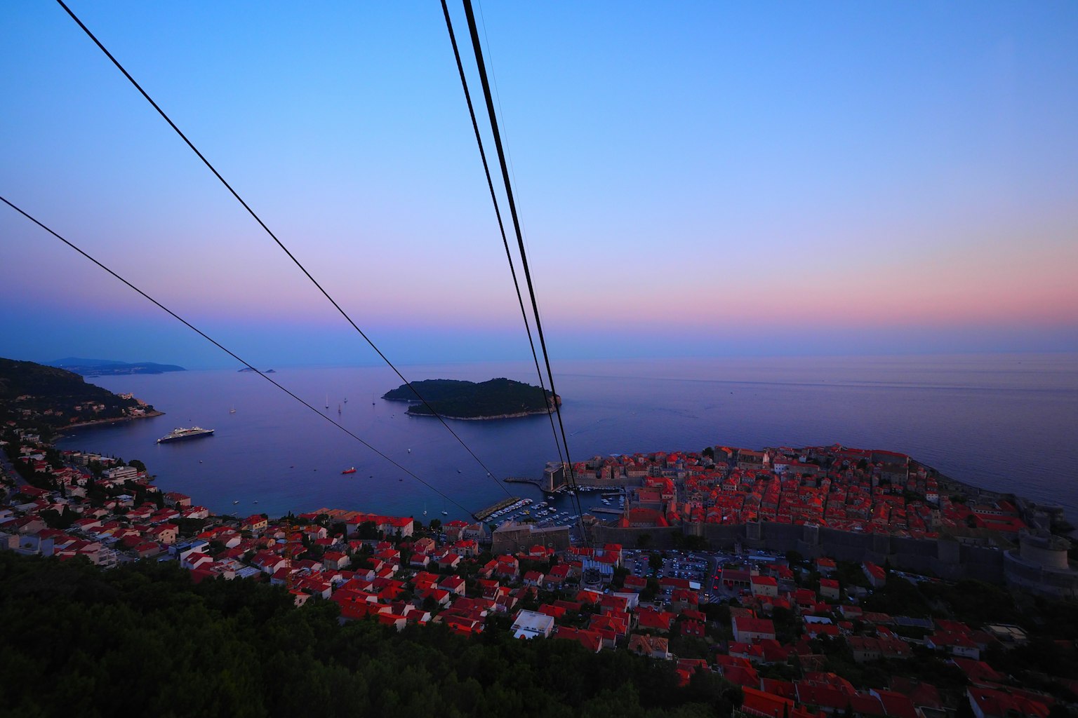 Schöner Dämmerungsblick auf das Meer und die Insel Seilbahnkabel, die den Himmel überqueren