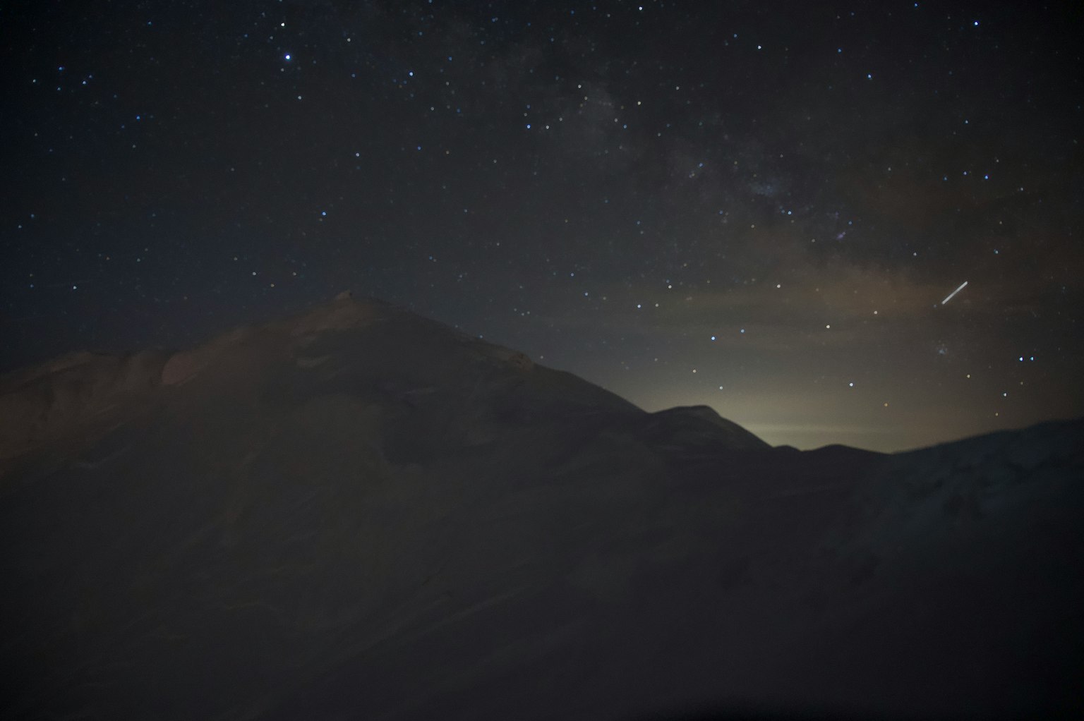 Silhouette d'une montagne sous un ciel étoilé avec une lumière lointaine