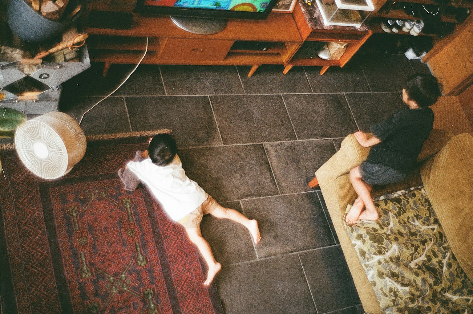 子供が床に寝転がり、もう一人の子供がソファに座っているリビングルームの風景