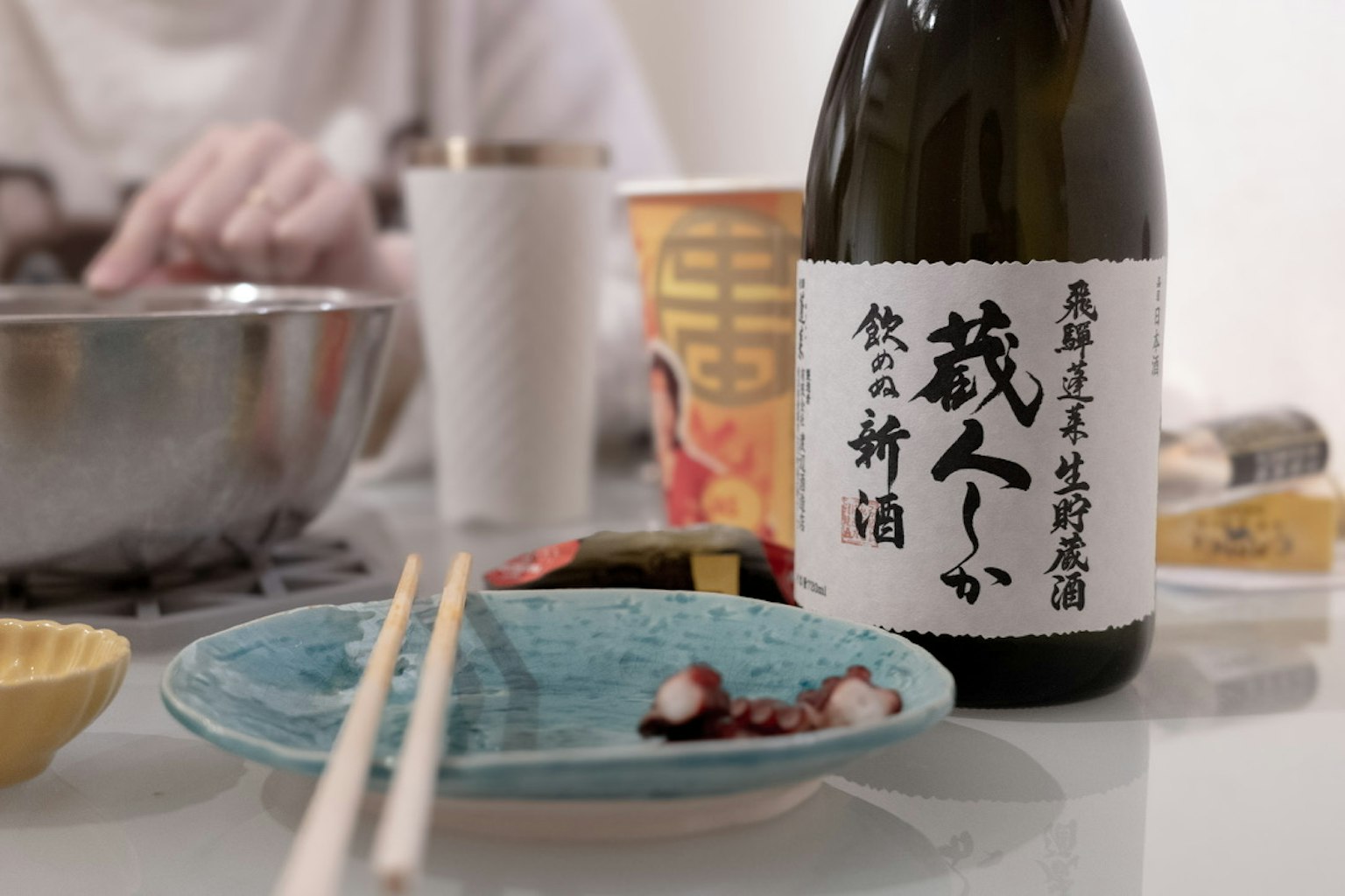 Un plato azul con pulpo y una botella de sake en la mesa
