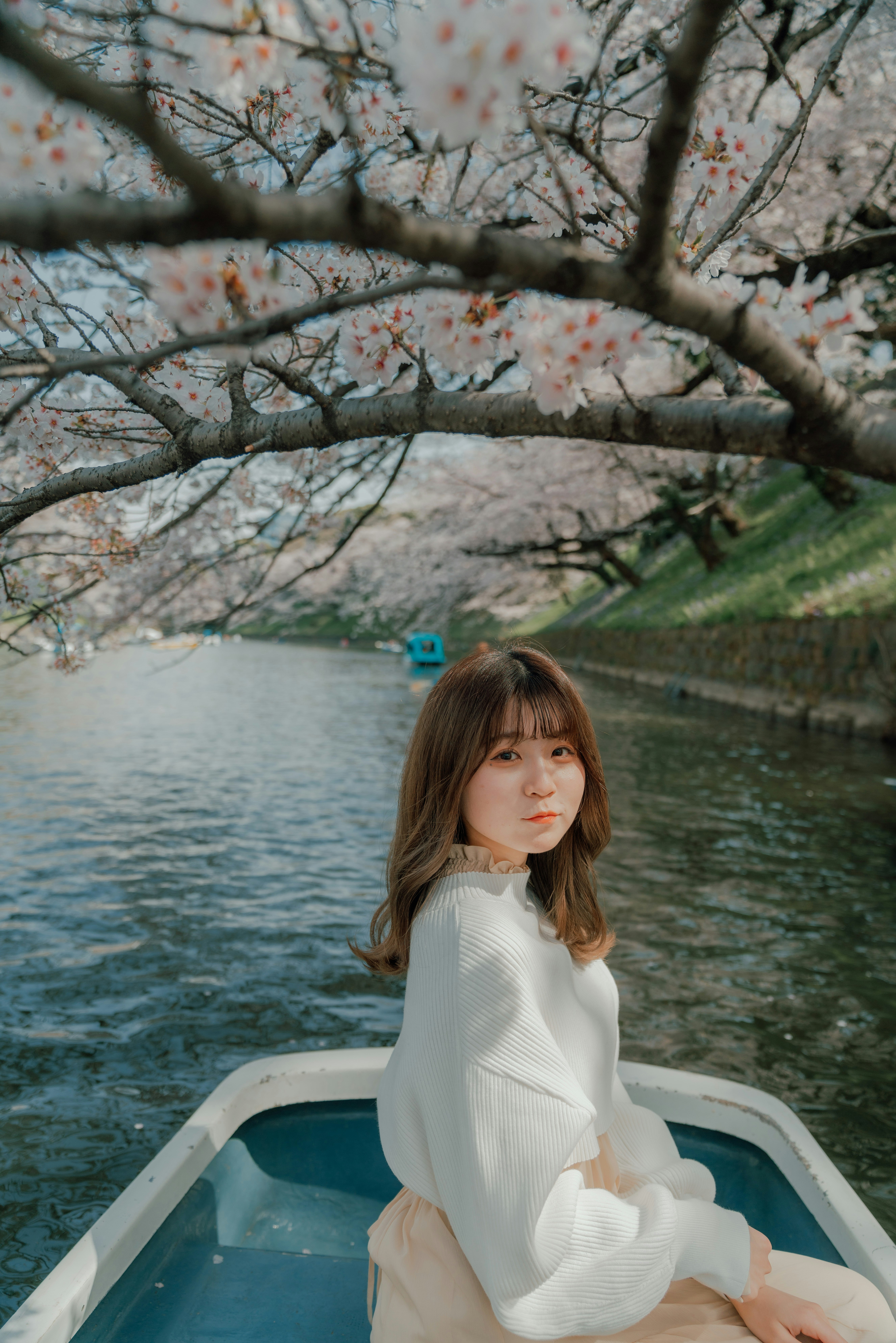 桜の枝が覆う小川沿いでボートに座る女性
