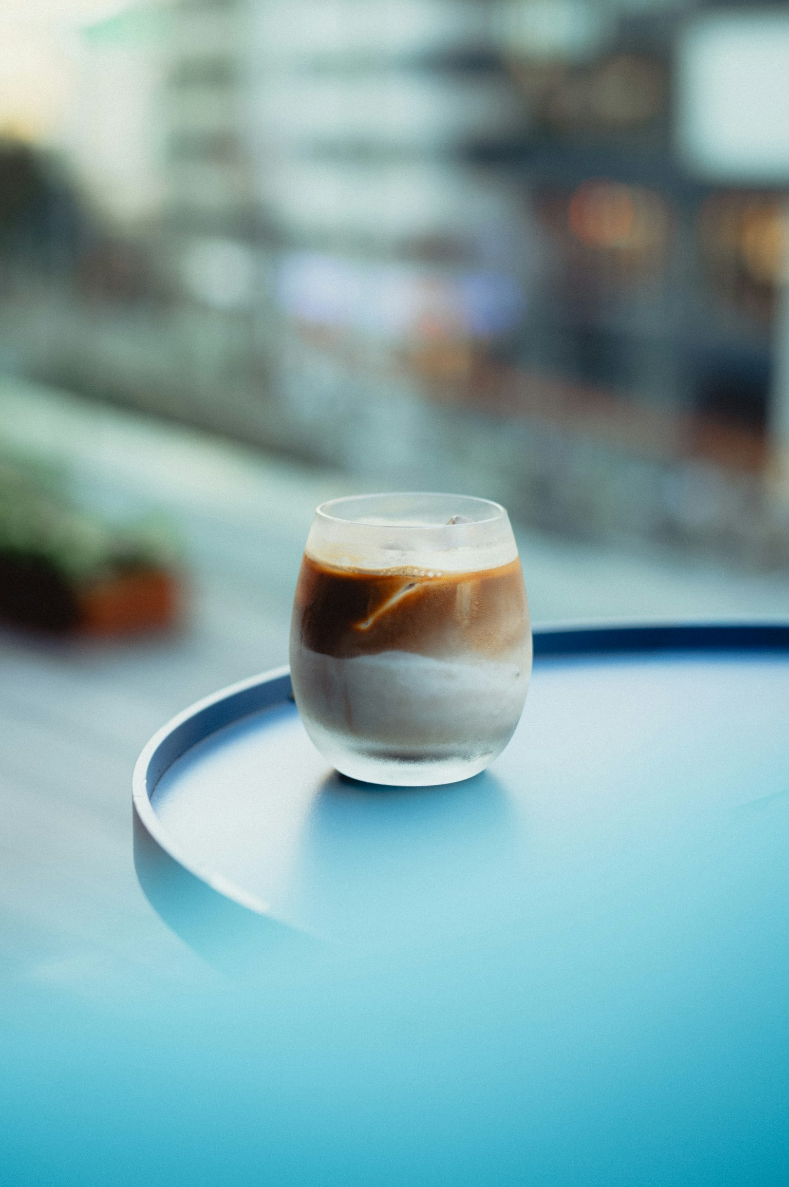 青いテーブルの上に置かれたアイスコーヒーのグラスがぼんやりとした背景の中にある