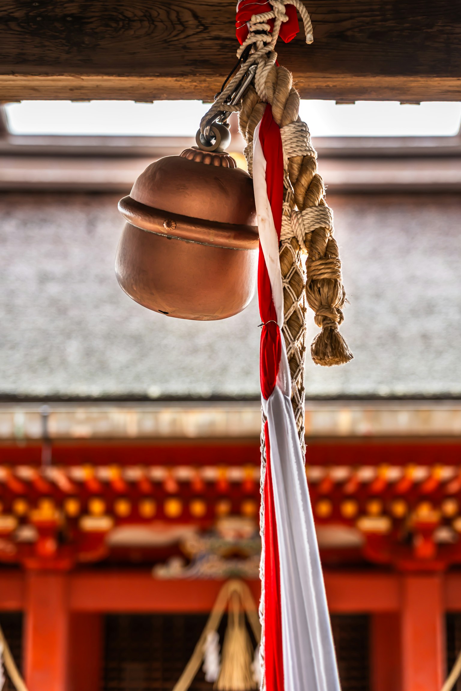 Une cloche suspendue avec shime-nawa rouge et blanc dans un sanctuaire