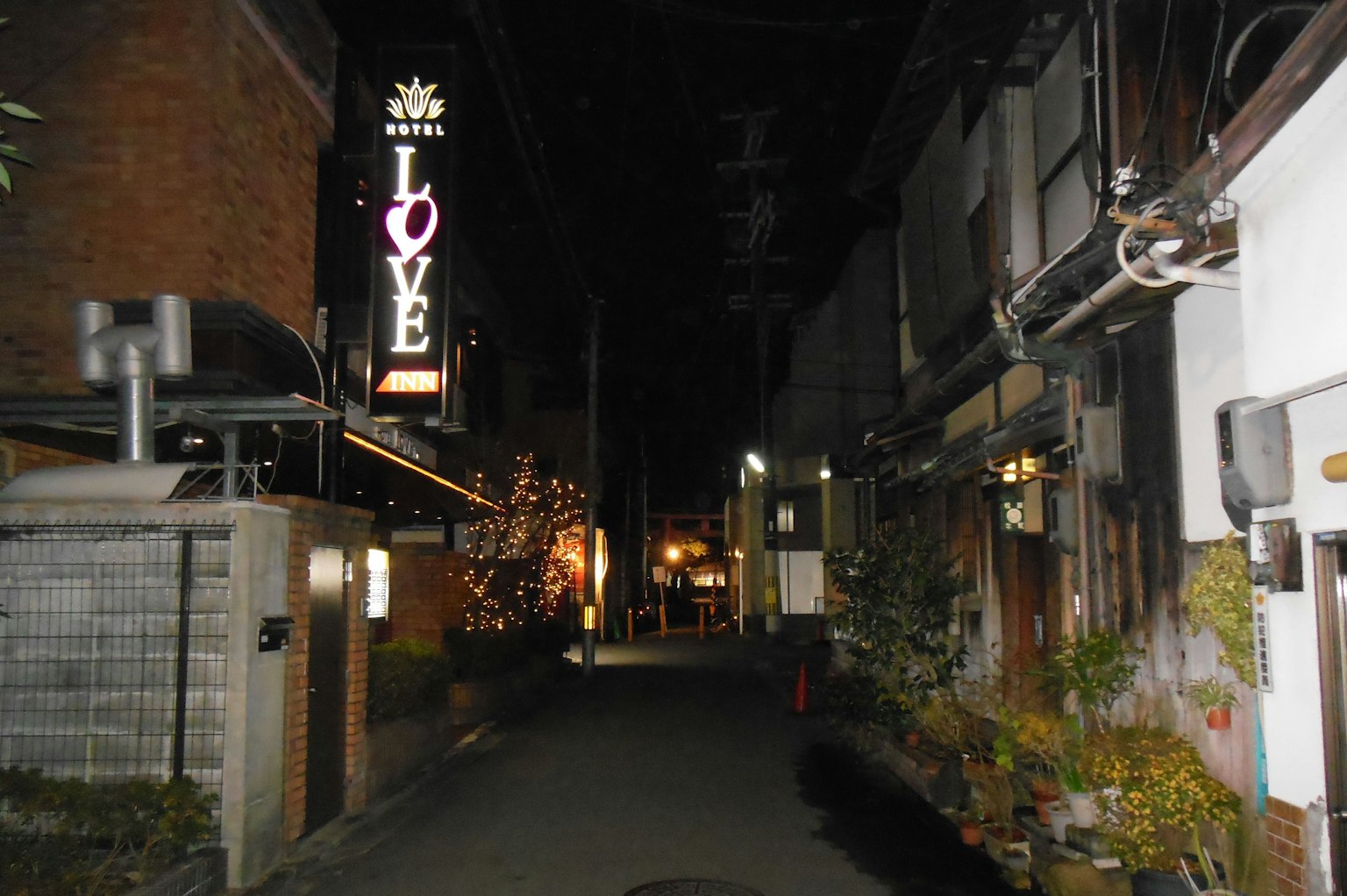 Schmale Gasse bei Nacht mit einem Neonschild LOVE und traditionellen Gebäuden