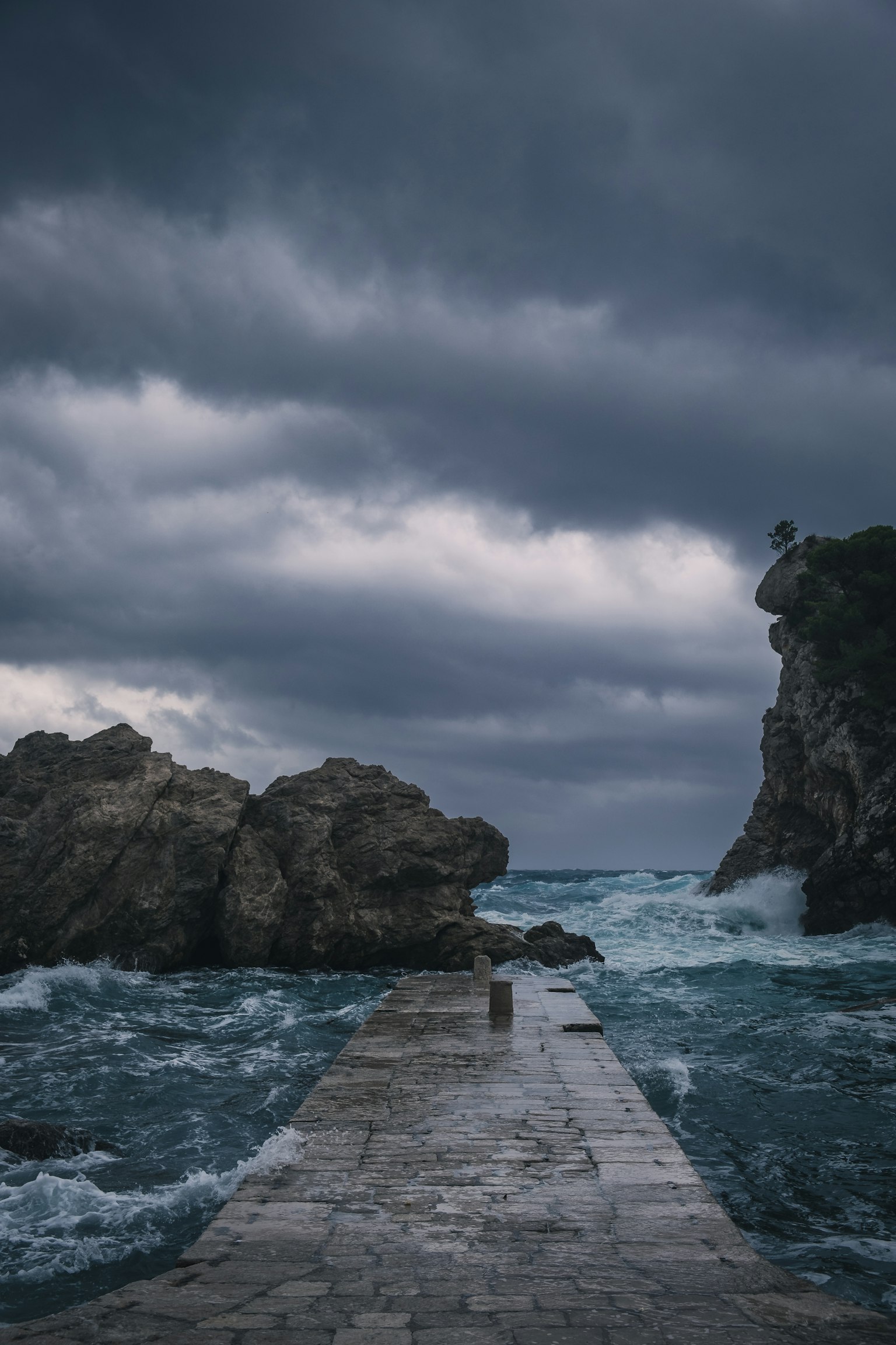 Quai en pierre s'étendant dans une mer agitée sous des nuages sombres