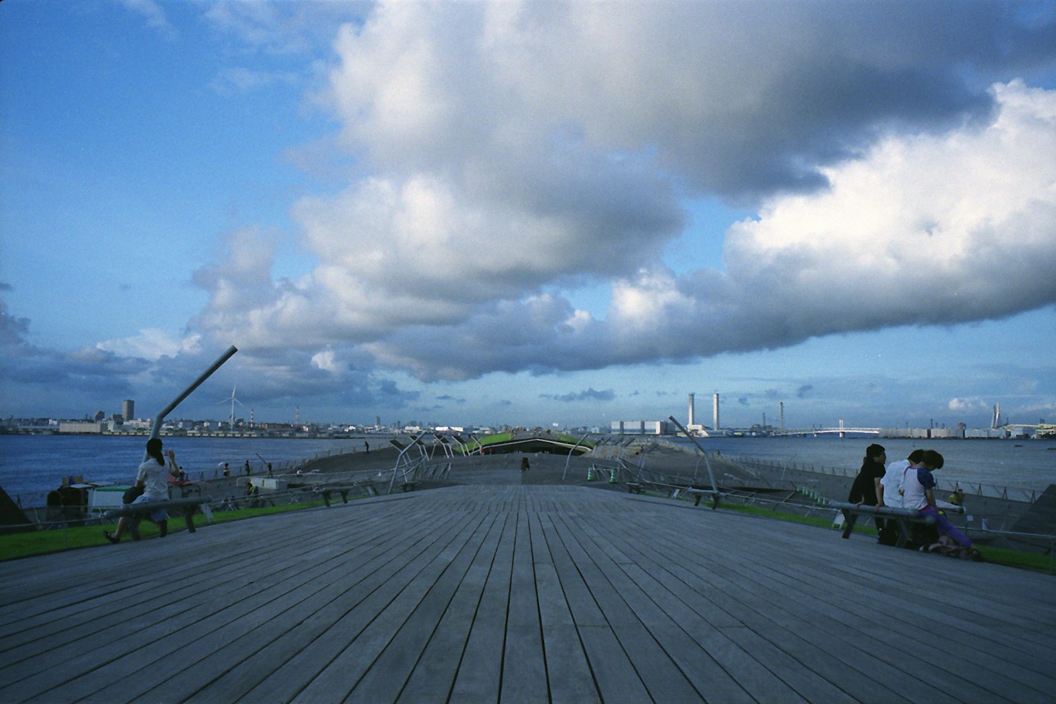 People sitting on a seaside promenade under a blue sky with clouds