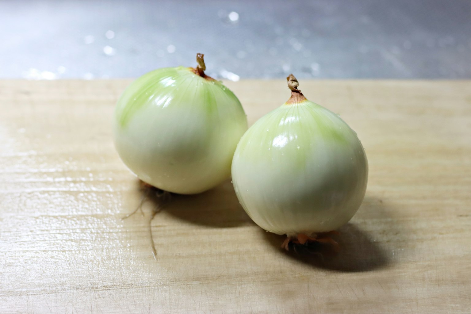 Shiny greenish-white pearl onions placed on a wooden cutting board
