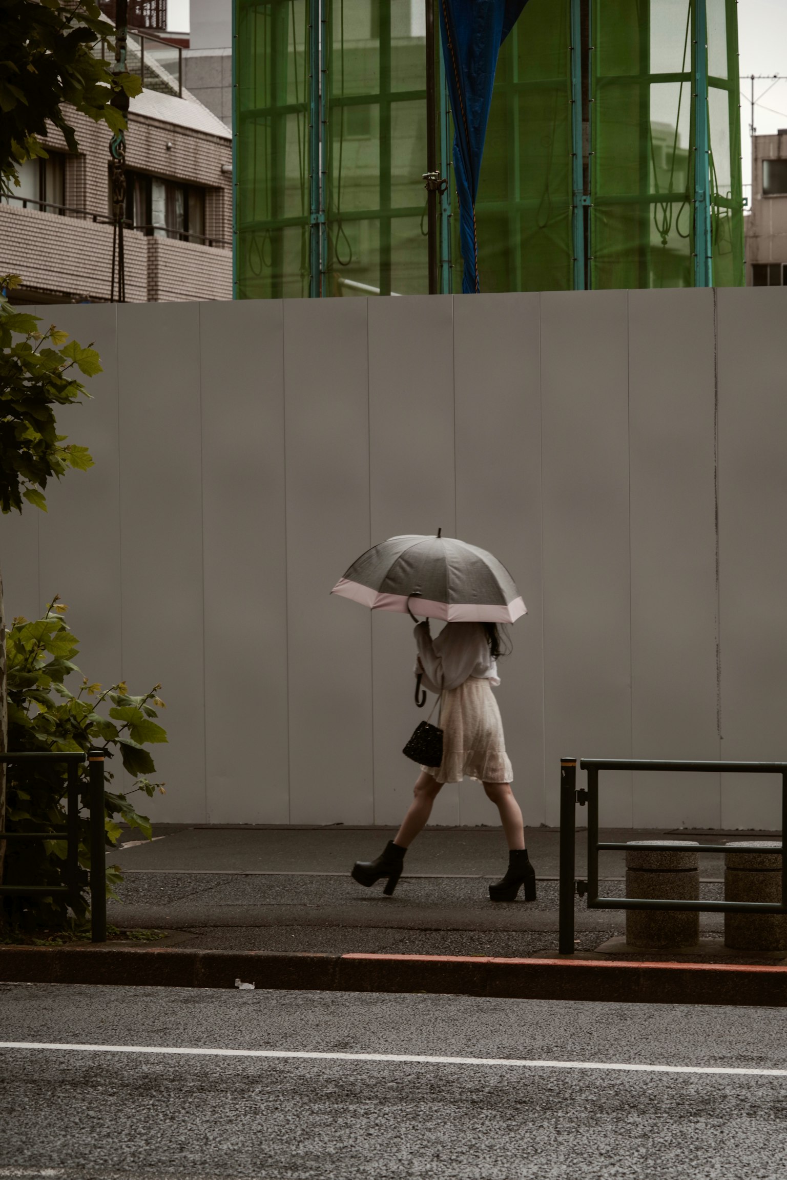 手持雨伞在城市街道上行走的女性 背景中有绿色建筑