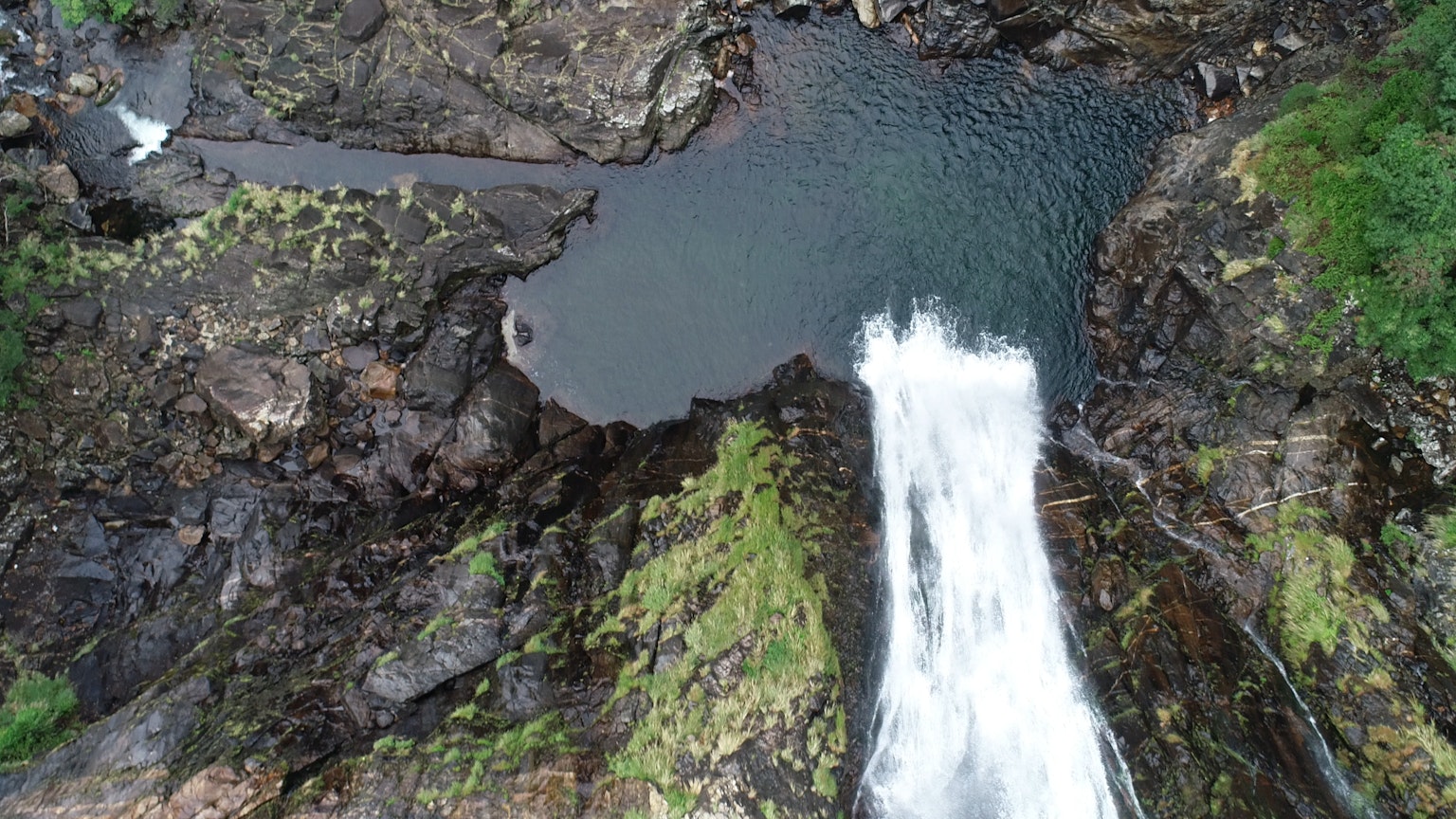 Ein Wasserfall, der von felsigen Klippen herabstürzt mit Blick von oben grünes Moos auf den Felsen