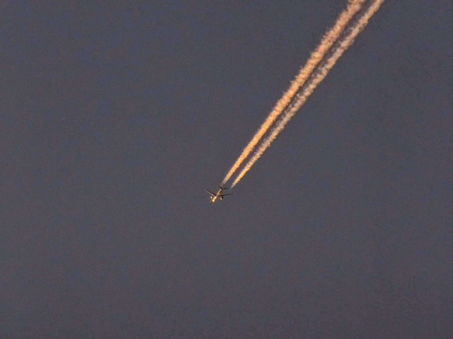夕暮れの空に伸びるオレンジ色の飛行機雲