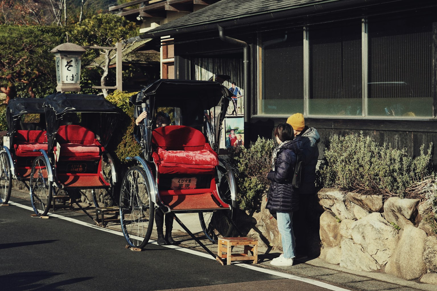 兩個人站在風景如畫的街道上的紅色人力車旁