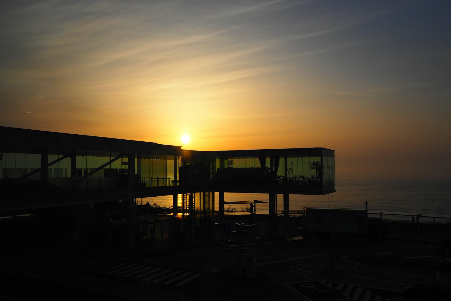 Glass building against the backdrop of a sunset over the sea