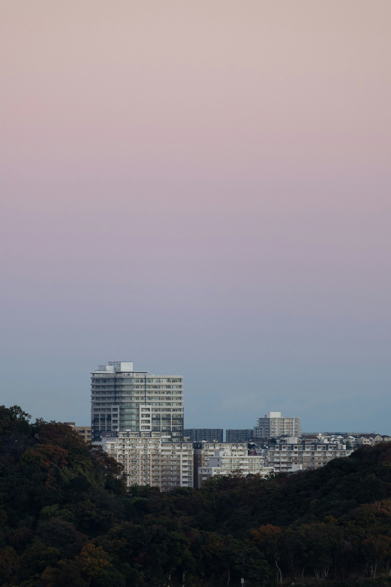 ทิวทัศน์เมืองที่มีตึกสูงอยู่เบื้องหลังท้องฟ้ายามพระอาทิตย์ตกสีชมพูอ่อน