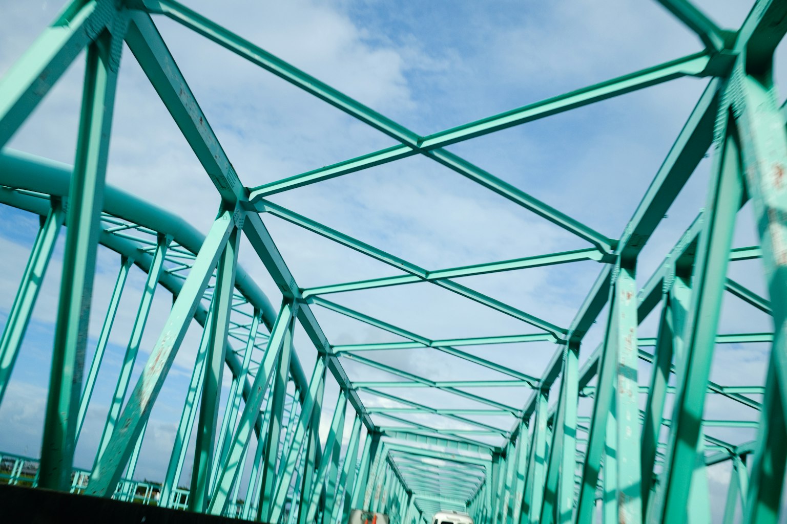 Vista desde debajo de un puente de metal turquesa con cielo azul y nubes