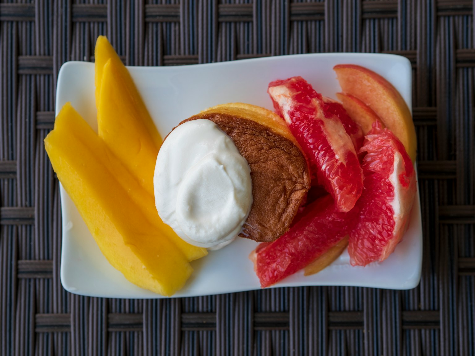 Un piatto con fette di mango e pompelmo accanto a una pasta guarnita di panna