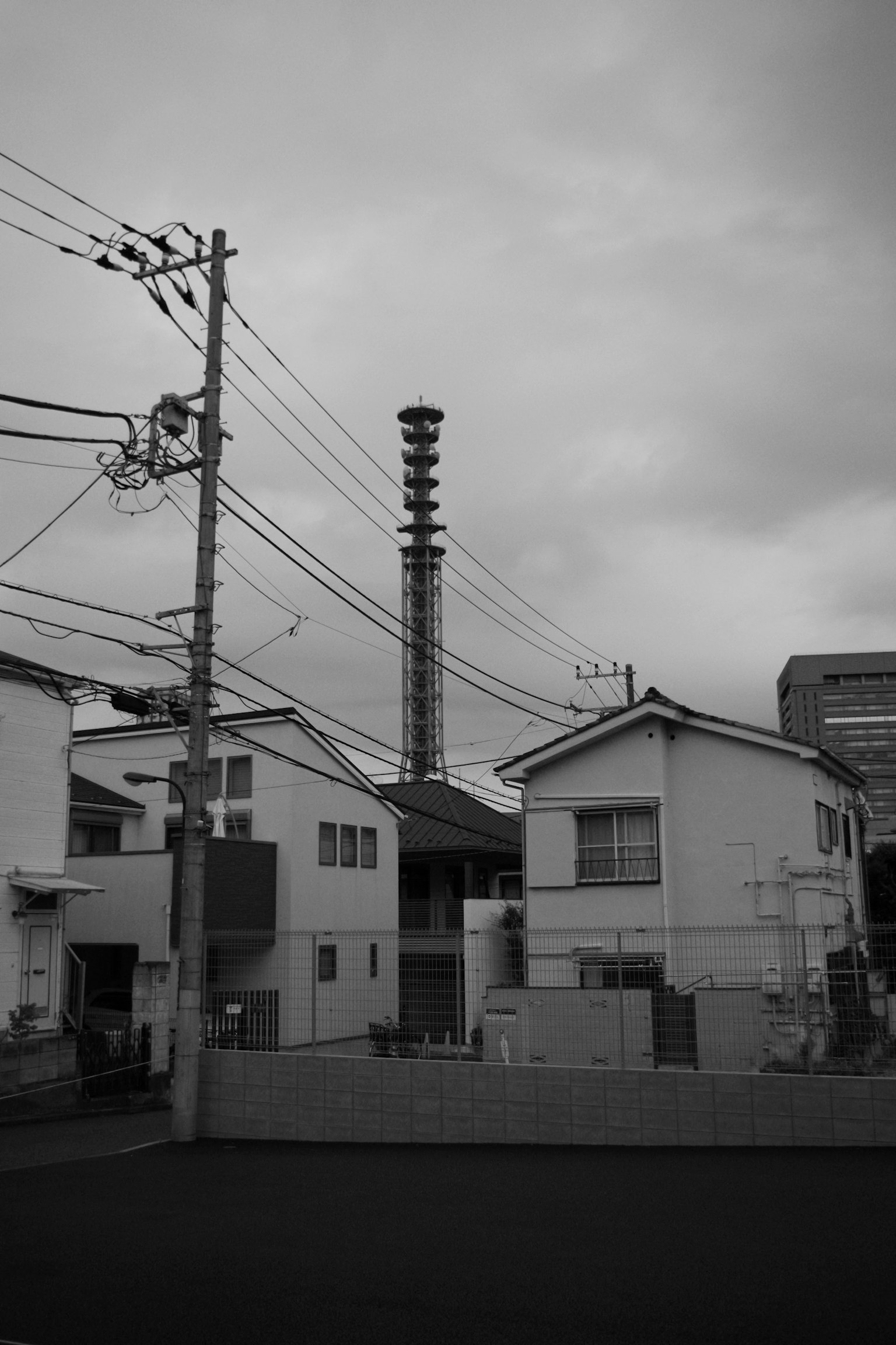 ภูมิทัศน์เมืองขาวดำที่มีเสาไฟฟ้าและบ้านใต้ท้องฟ้ามืดครึ้มพร้อมปล่องไฟโรงงาน