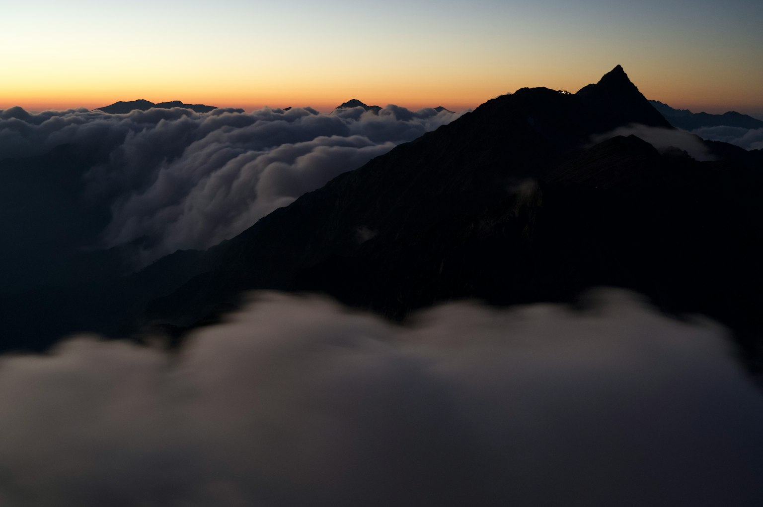 Silhouette of a mountain rising above clouds at sunset
