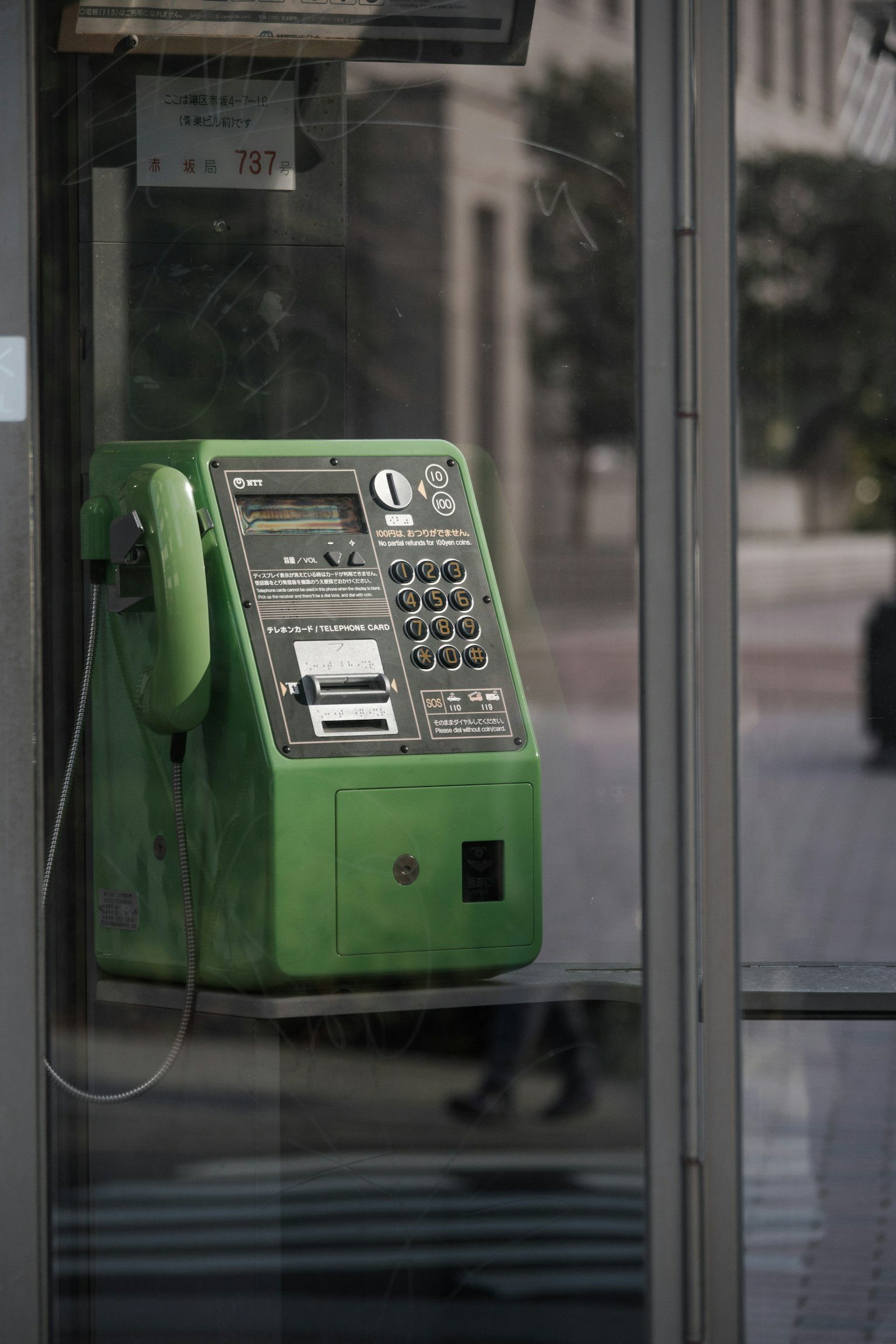 Telefono pubblico verde installato in una cabina telefonica in vetro