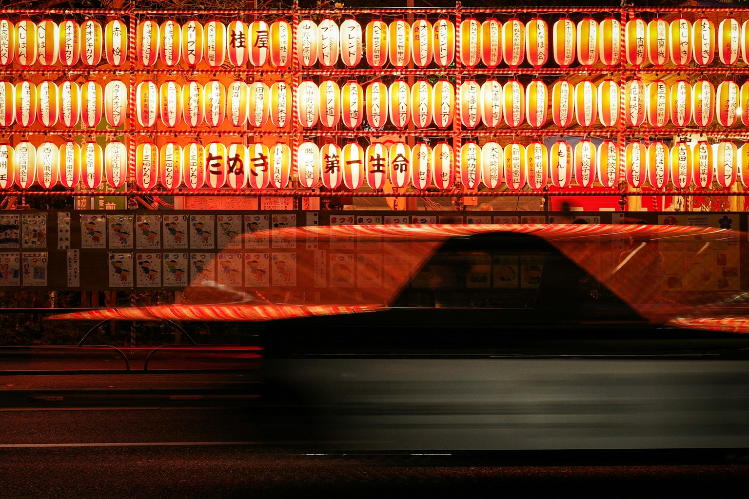 Silhouette of a moving car against a backdrop of red lanterns